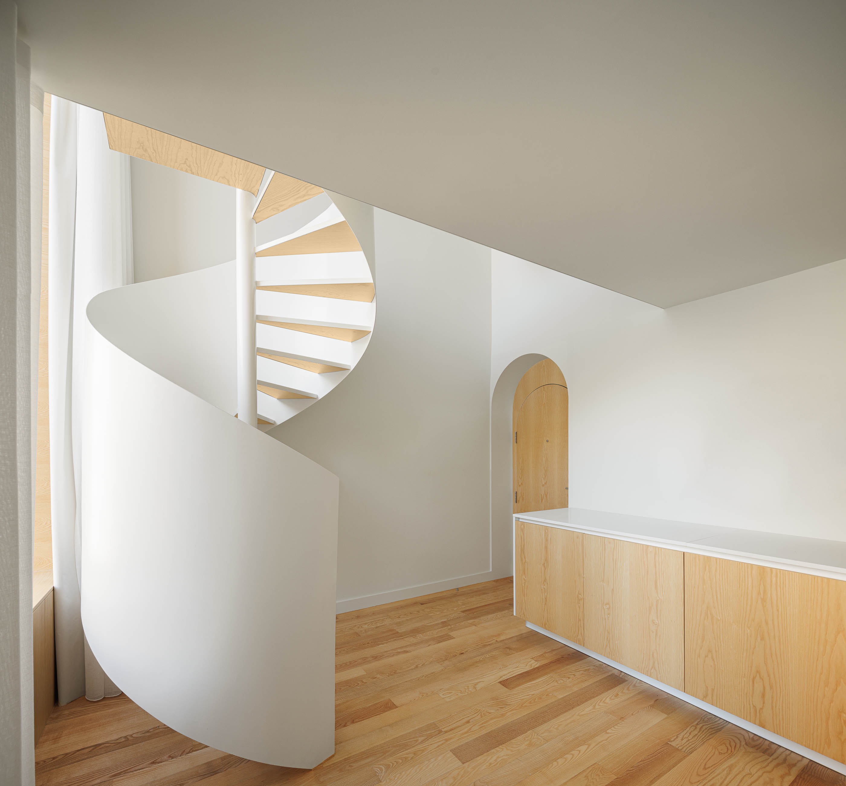 Escada em caracol branca, armários em madeira clara e porta em arco num espaço luminoso. — Boavista 339 arquitetura Paulo Merlini Architects em Porto
