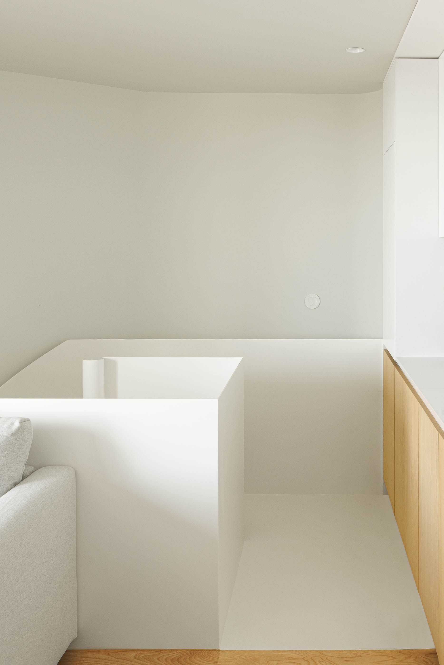 Espaço com elementos arquitetónicos brancos, sofá cinzento e armários em madeira clara. — Boavista 339 arquitetura Paulo Merlini Architects em Porto
