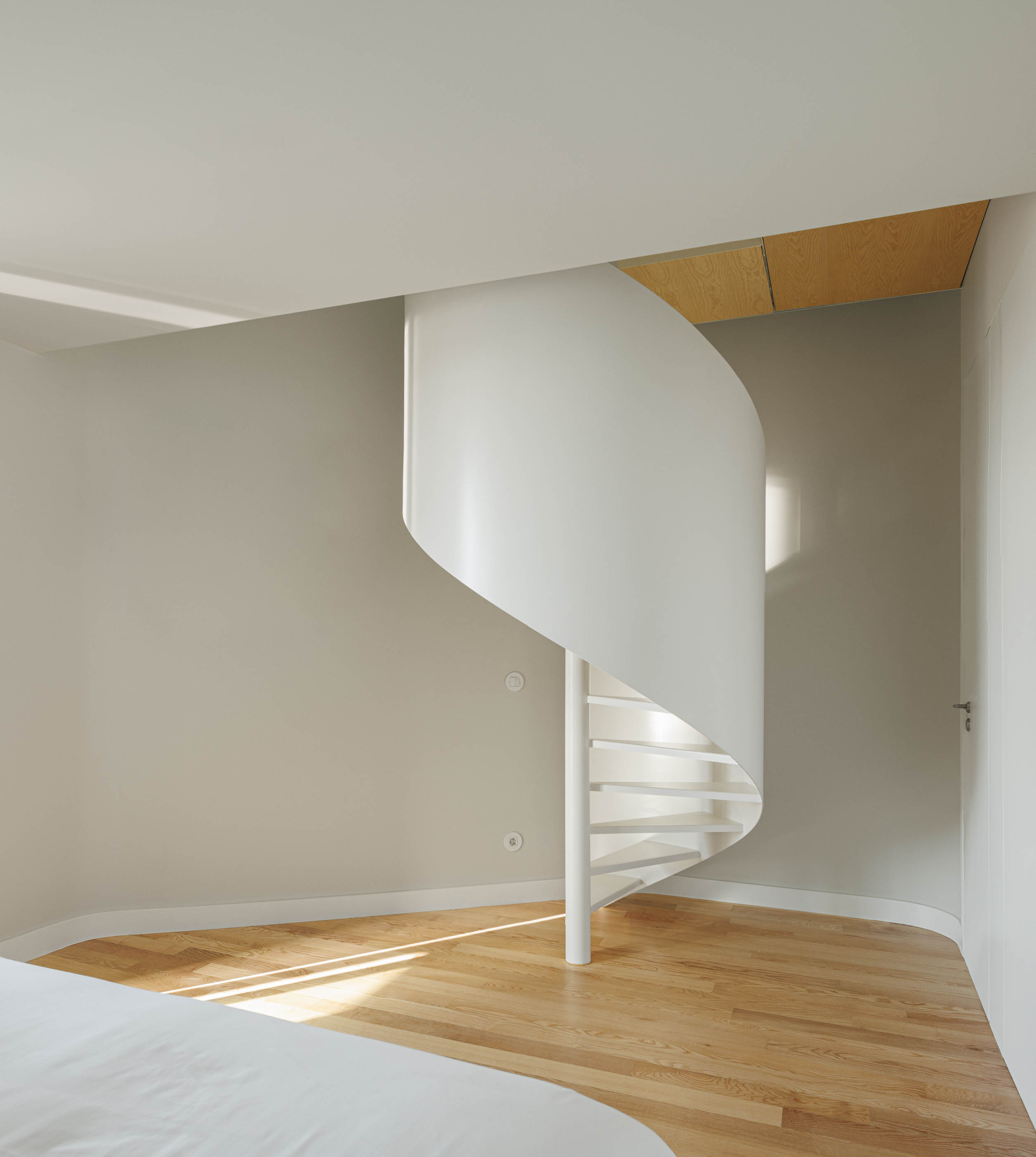 Escada em caracol branca num quarto com pavimento em madeira e luz natural. — Boavista 339 arquitetura Paulo Merlini Architects em Porto