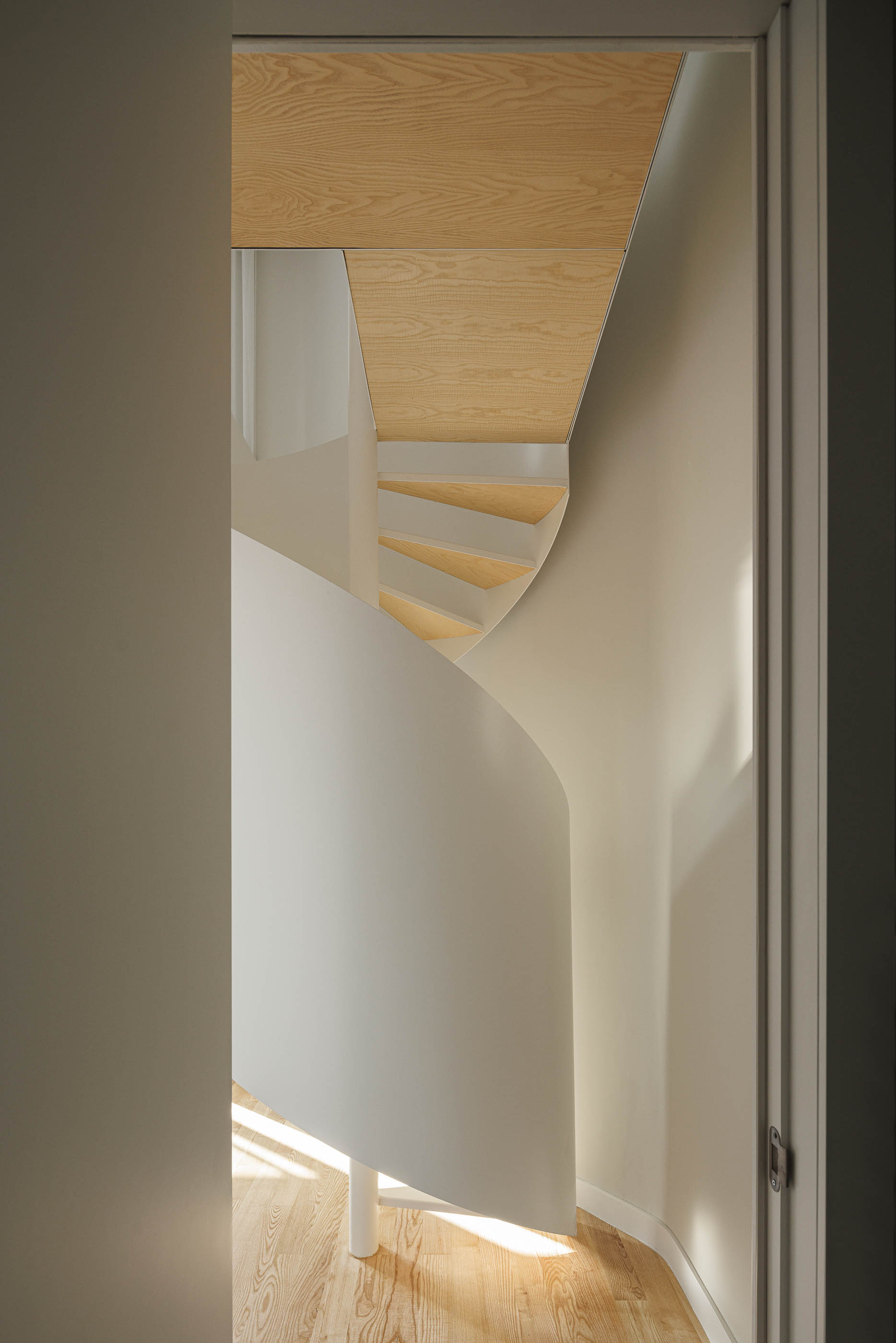Escada em caracol branca, vista através de uma porta, com luz natural e pavimento em madeira. — Boavista 339 arquitetura Paulo Merlini Architects em Porto