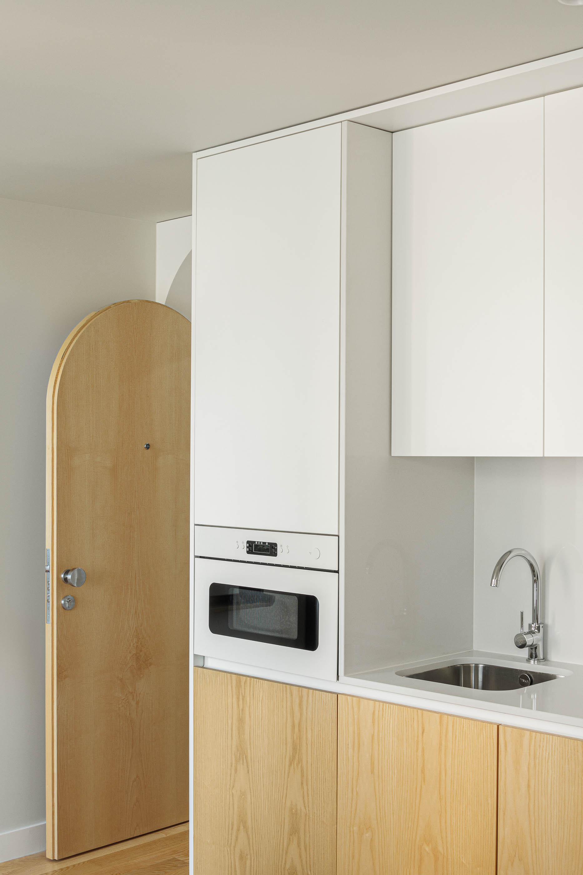 Detalhe da cozinha com armários brancos e madeira clara, porta em arco e lava-loiça. — Boavista 339 arquitetura Paulo Merlini Architects em Porto