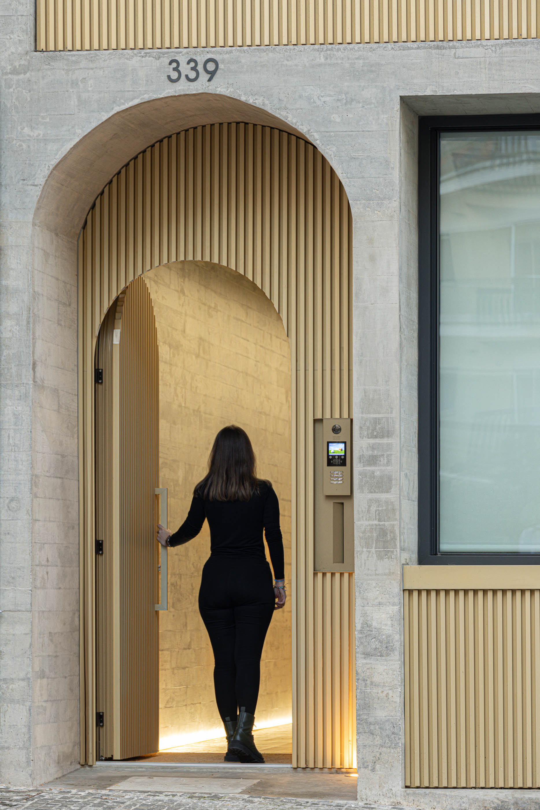 Mulher a entrar no edifício "Boavista 339" pela porta em arco com revestimento em ripas verticais. — Boavista 339 arquitetura Paulo Merlini Architects em Porto