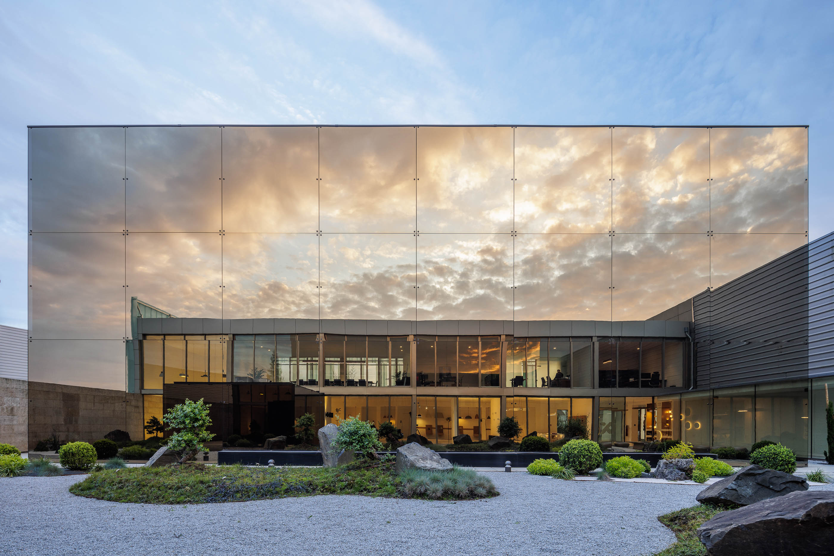 Exterior: Fachada espelhada refletindo o céu e o jardim zen, com iluminação indireta. — Requalificação e Ampliação das Instalações Exporlux arquitetura Espaço Objecto em Águeda