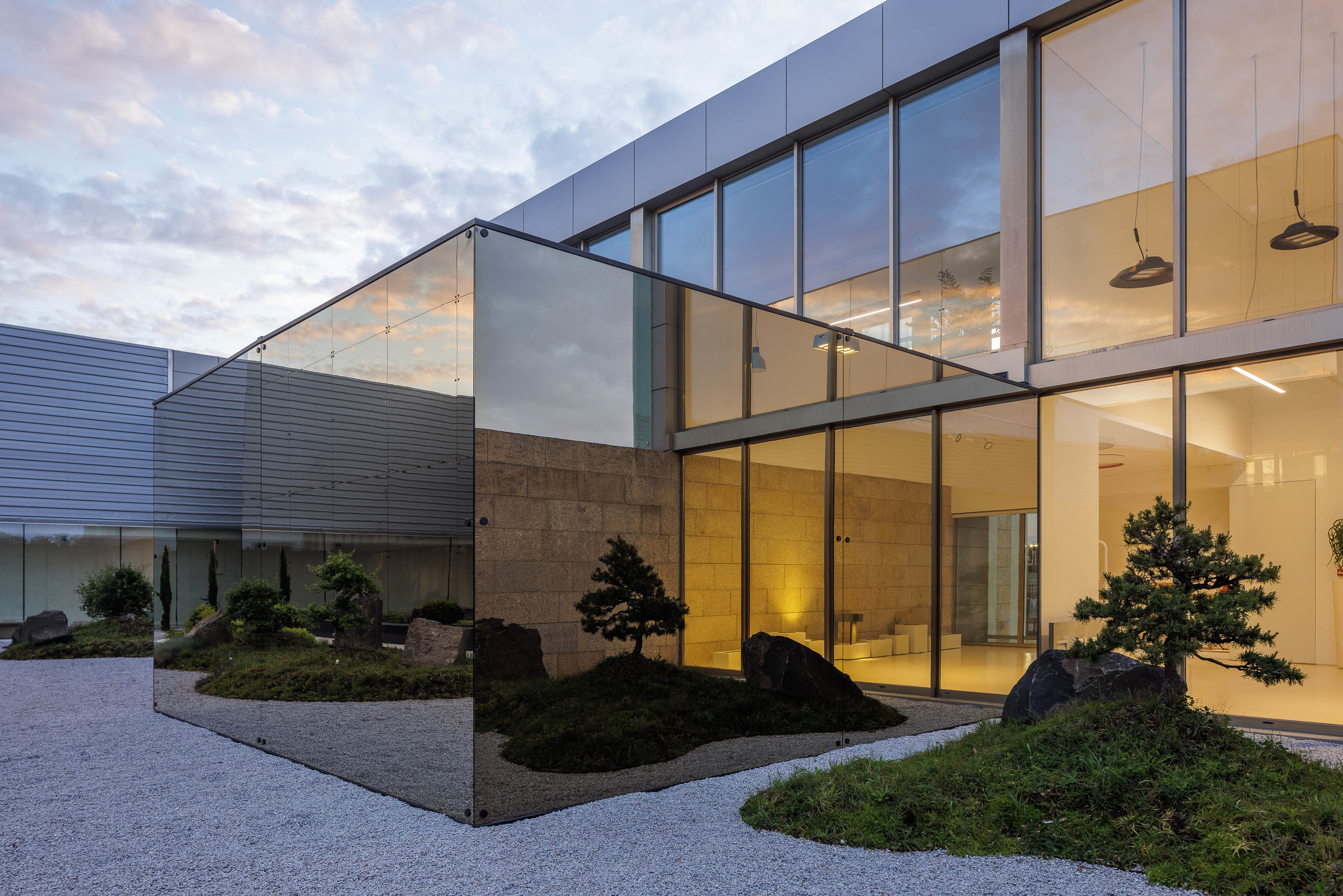 Exterior: Edifício com fachada espelhada e jardim zen, com iluminação indireta. — Requalificação e Ampliação das Instalações Exporlux arquitetura Espaço Objecto em Águeda