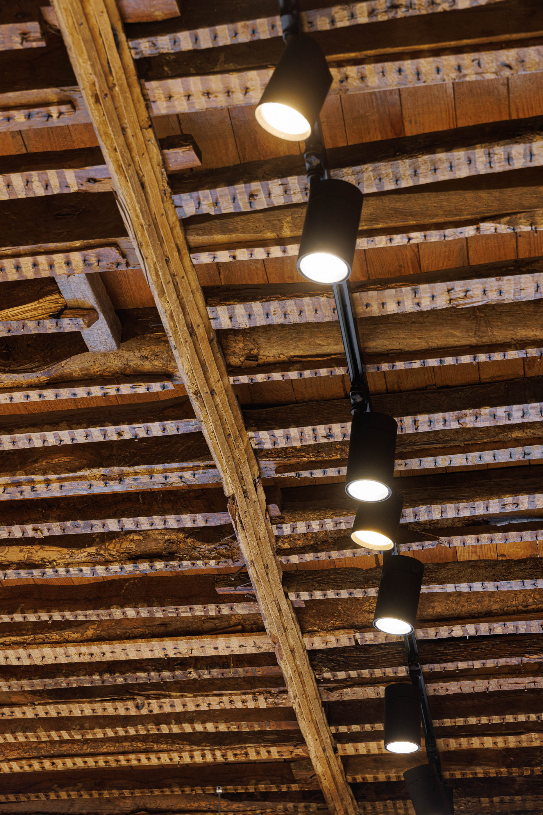 Teto: Detalhe do teto em madeira rústica com vigas e candeeiros cilíndricos pretos. — Jorge Oculista arquitetura Inception Architects Studio em Braga