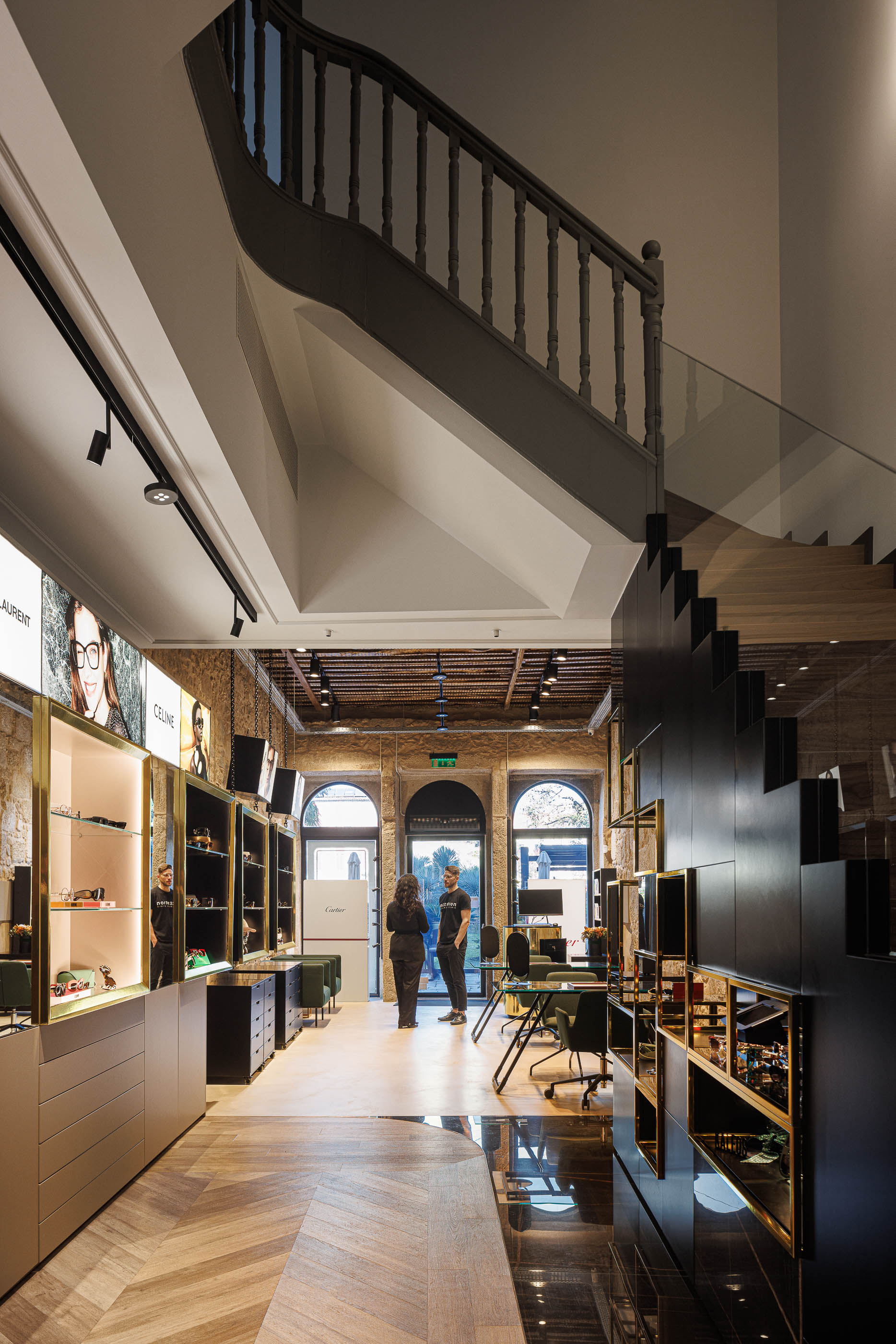 Loja: Vista da loja com escadas, expositores de óculos e clientes a circular no espaço. — Jorge Oculista arquitetura Inception Architects Studio em Braga