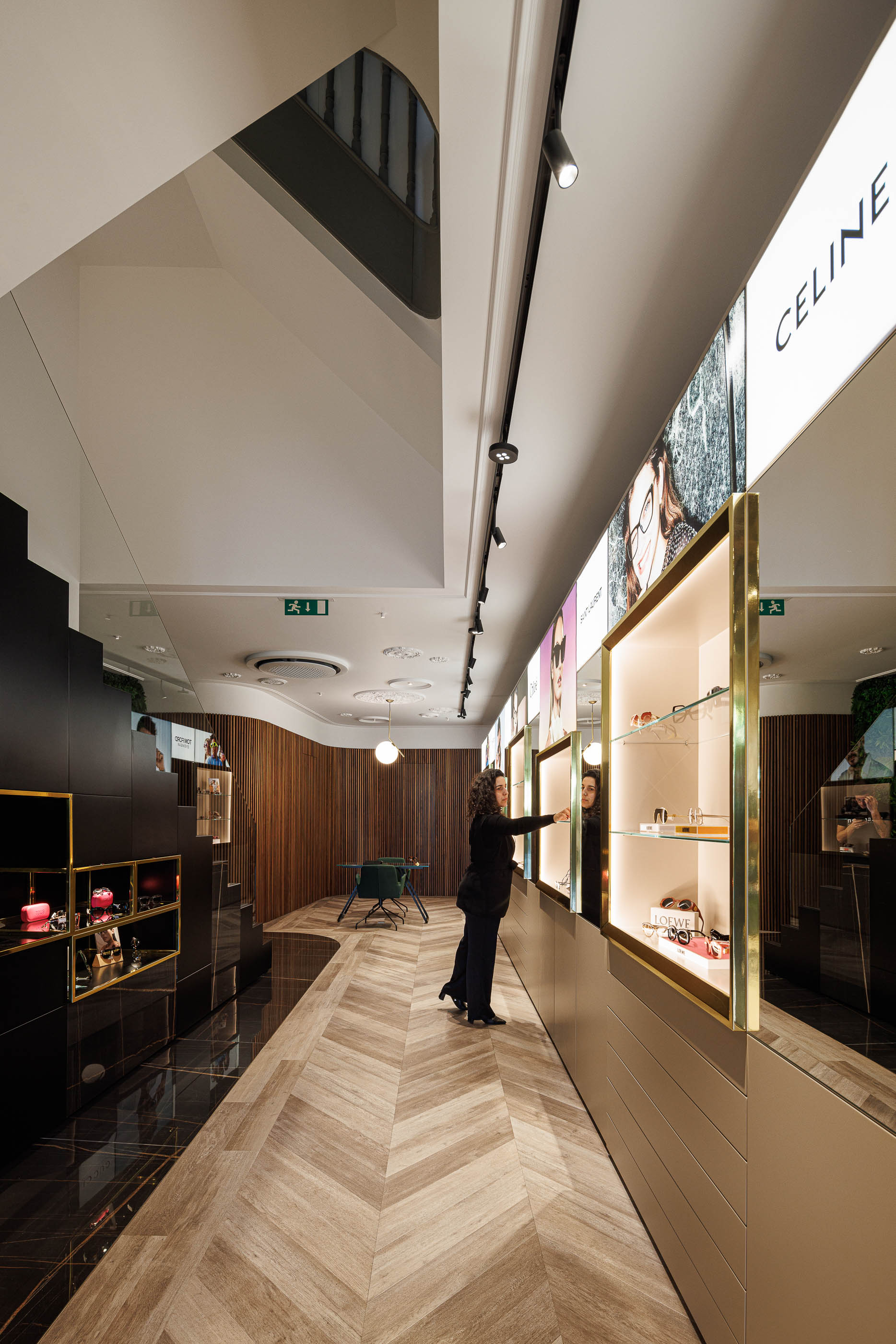 Loja: Corredor com expositores de óculos, pavimento em espinha de peixe e zona de atendimento ao fundo. — Jorge Oculista arquitetura Inception Architects Studio em Braga