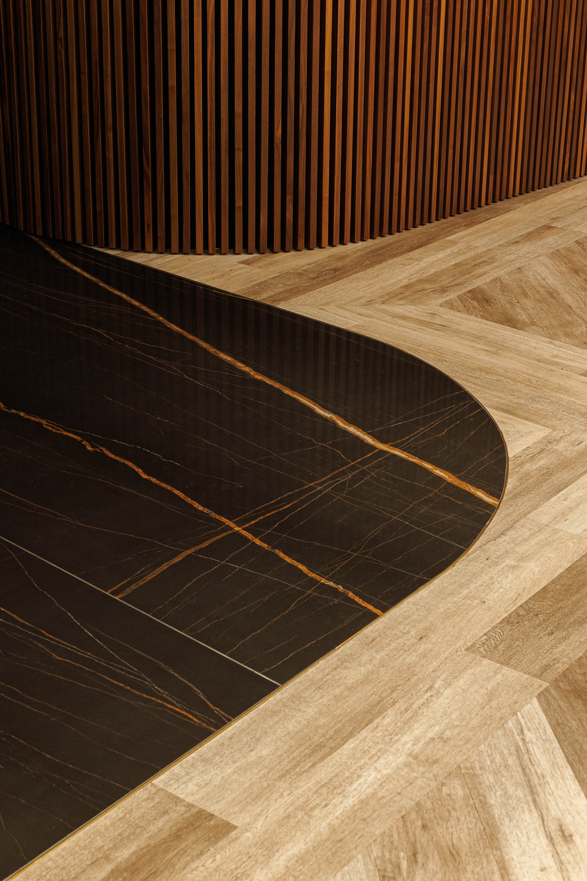 Detalhe: Pavimento em madeira e mármore preto com veios dourados, junto a painéis de madeira vertical. — Jorge Oculista arquitetura Inception Architects Studio em Braga