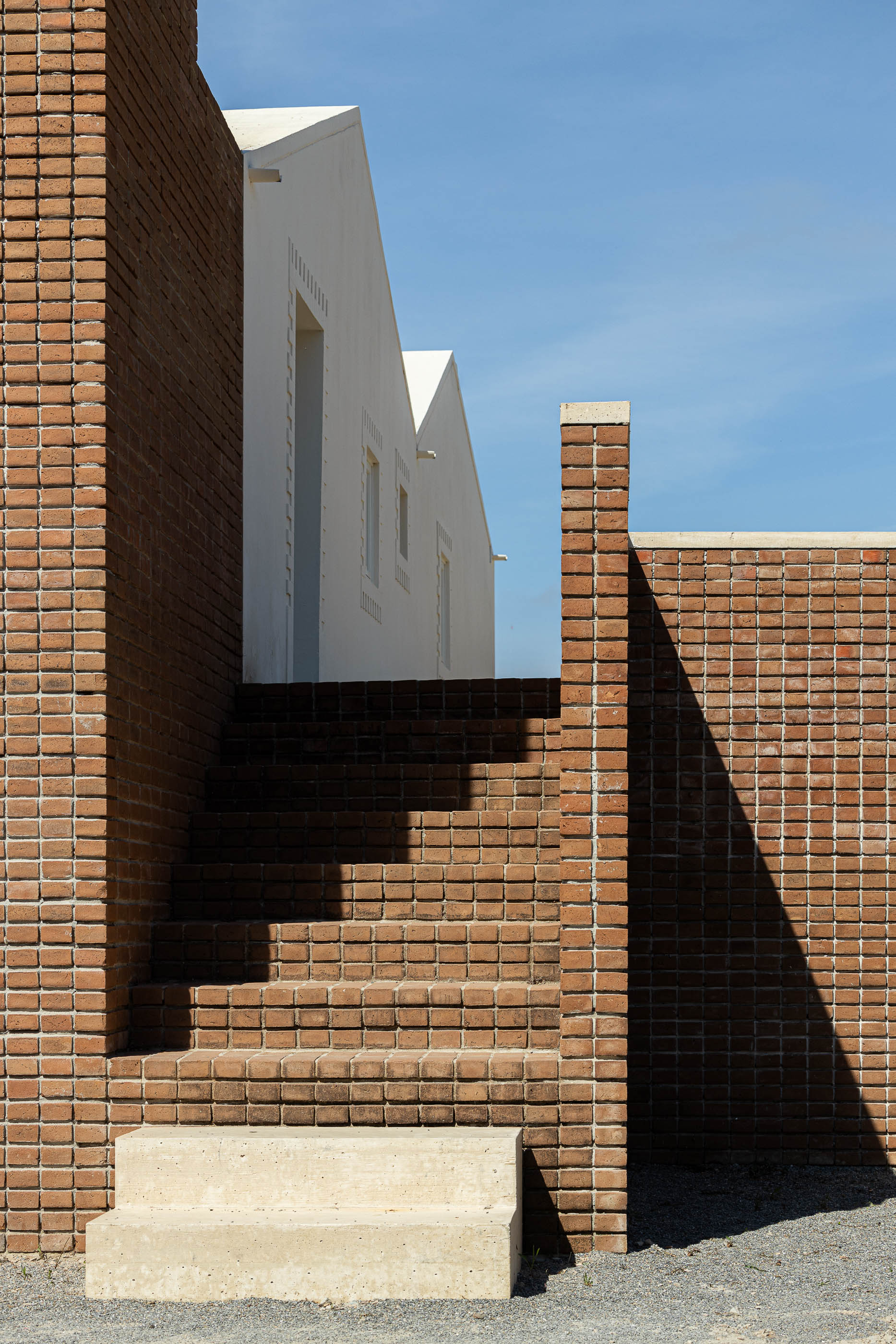 Escadaria exterior: Degraus de tijolo que levam a uma porta, com paredes de tijolo adjacentes. — Olaria Municipal arquitetura ARDE Arquitetura+Design em Odemira