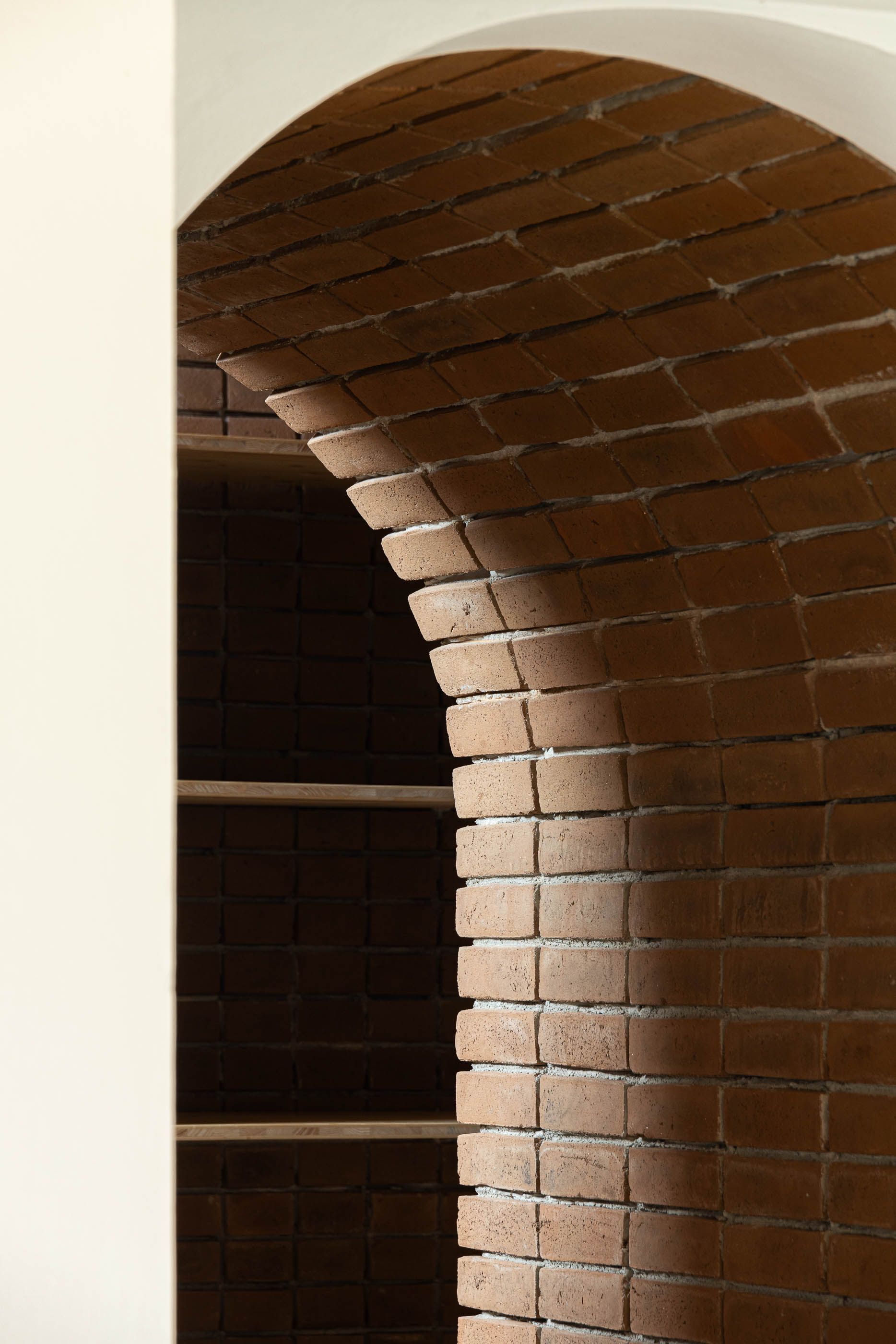 Corredor: Arco de tijolo com prateleiras de madeira ao fundo. — Olaria Municipal arquitetura ARDE Arquitetura+Design em Odemira