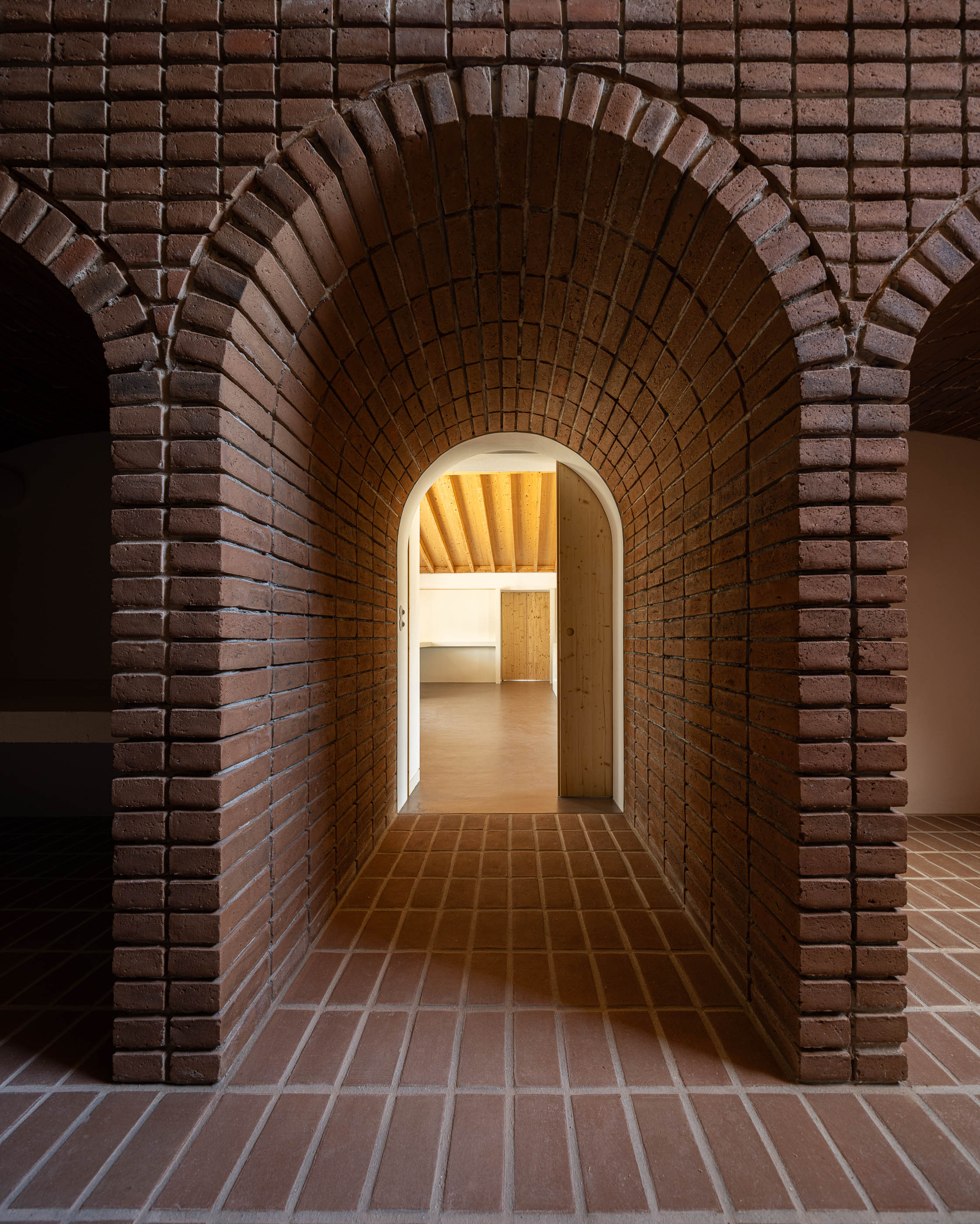 Corredor: Arcos de tijolo que dão acesso a um espaço interior com pavimento castanho. — Olaria Municipal arquitetura ARDE Arquitetura+Design em Odemira