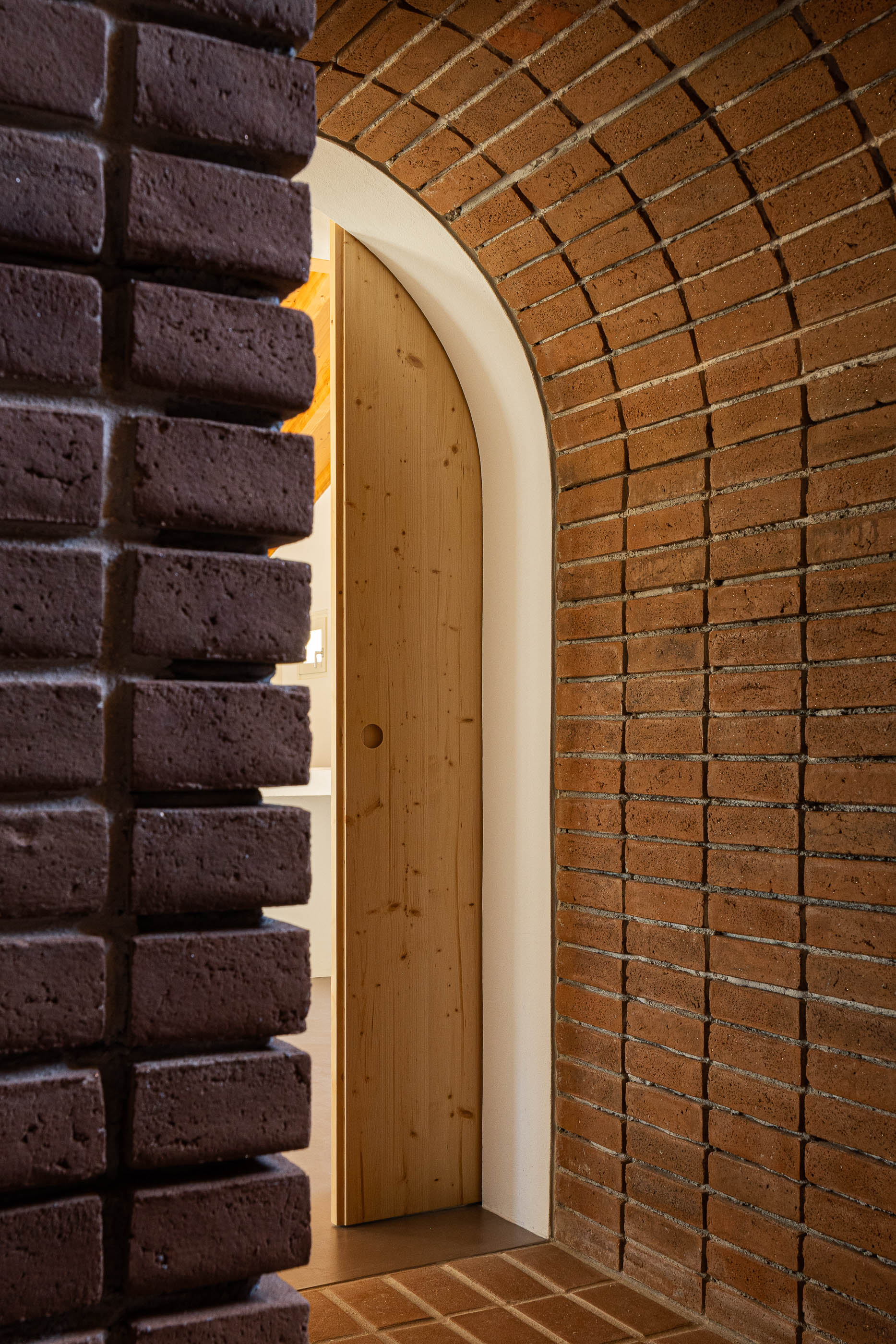 Corredor: Detalhe do arco de tijolo com porta de madeira ao fundo. — Olaria Municipal arquitetura ARDE Arquitetura+Design em Odemira