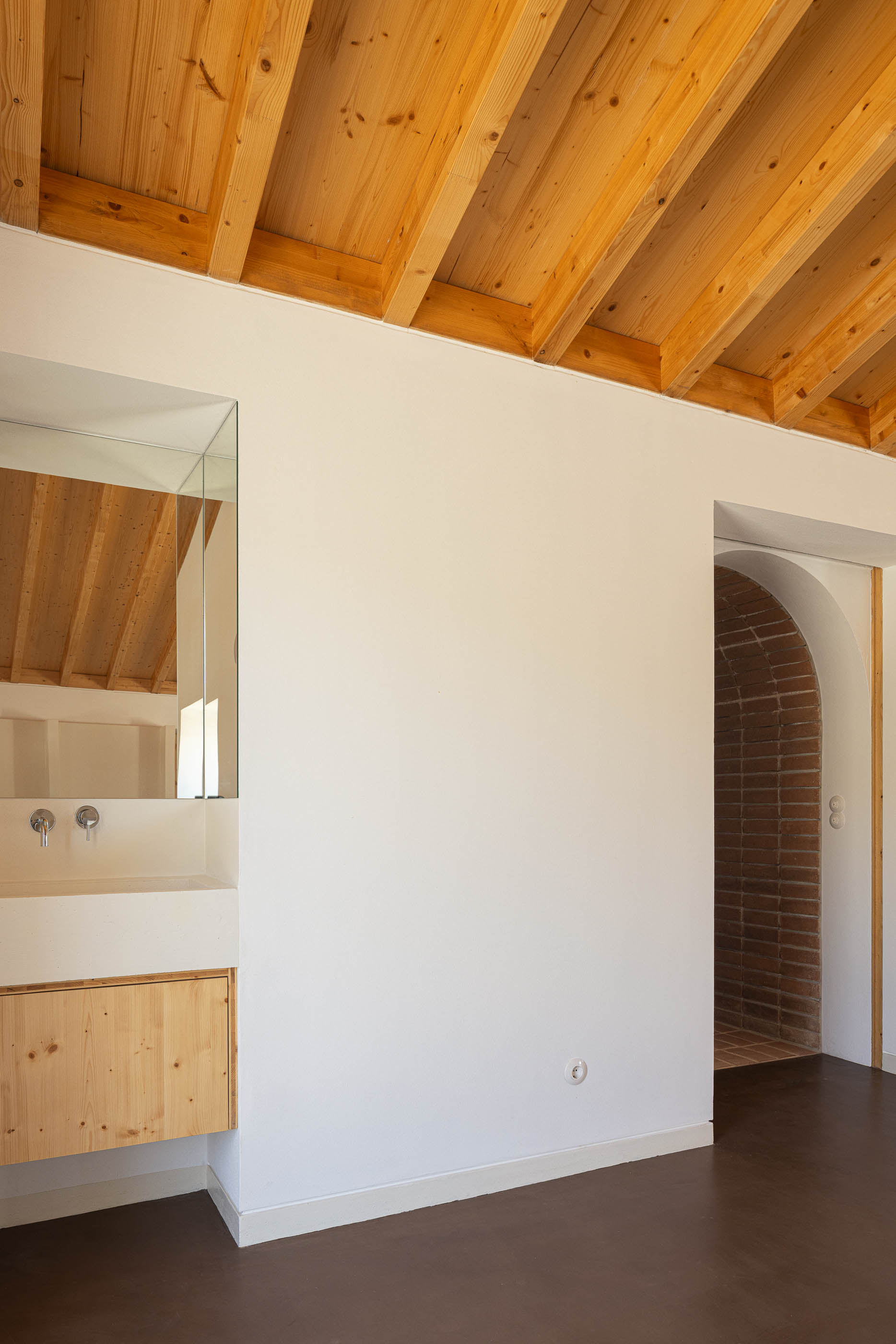 Casa de banho: Lavatório branco com espelho e teto de madeira, com porta para o corredor de tijolo. — Olaria Municipal arquitetura ARDE Arquitetura+Design em Odemira