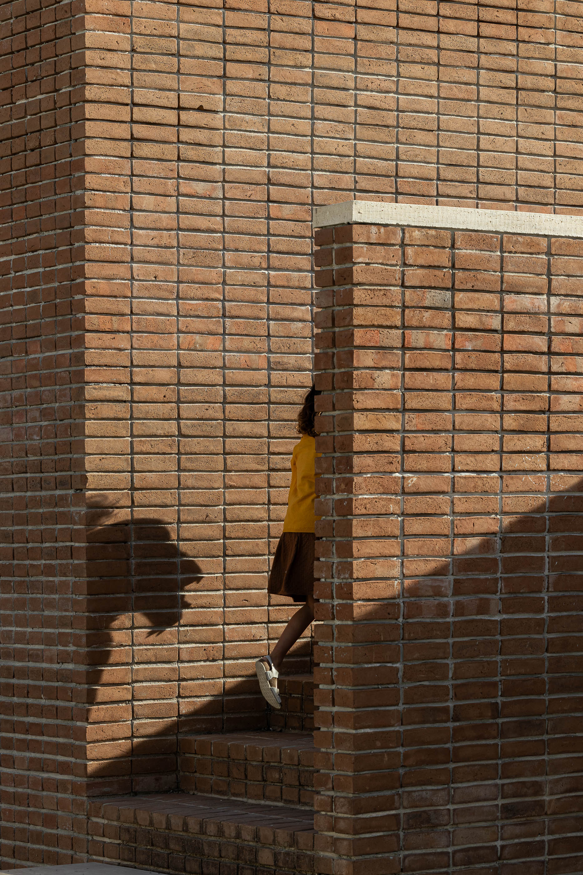 Escadaria exterior: Pessoa a subir escadas de tijolo, com paredes de tijolo adjacentes. — Olaria Municipal arquitetura ARDE Arquitetura+Design em Odemira