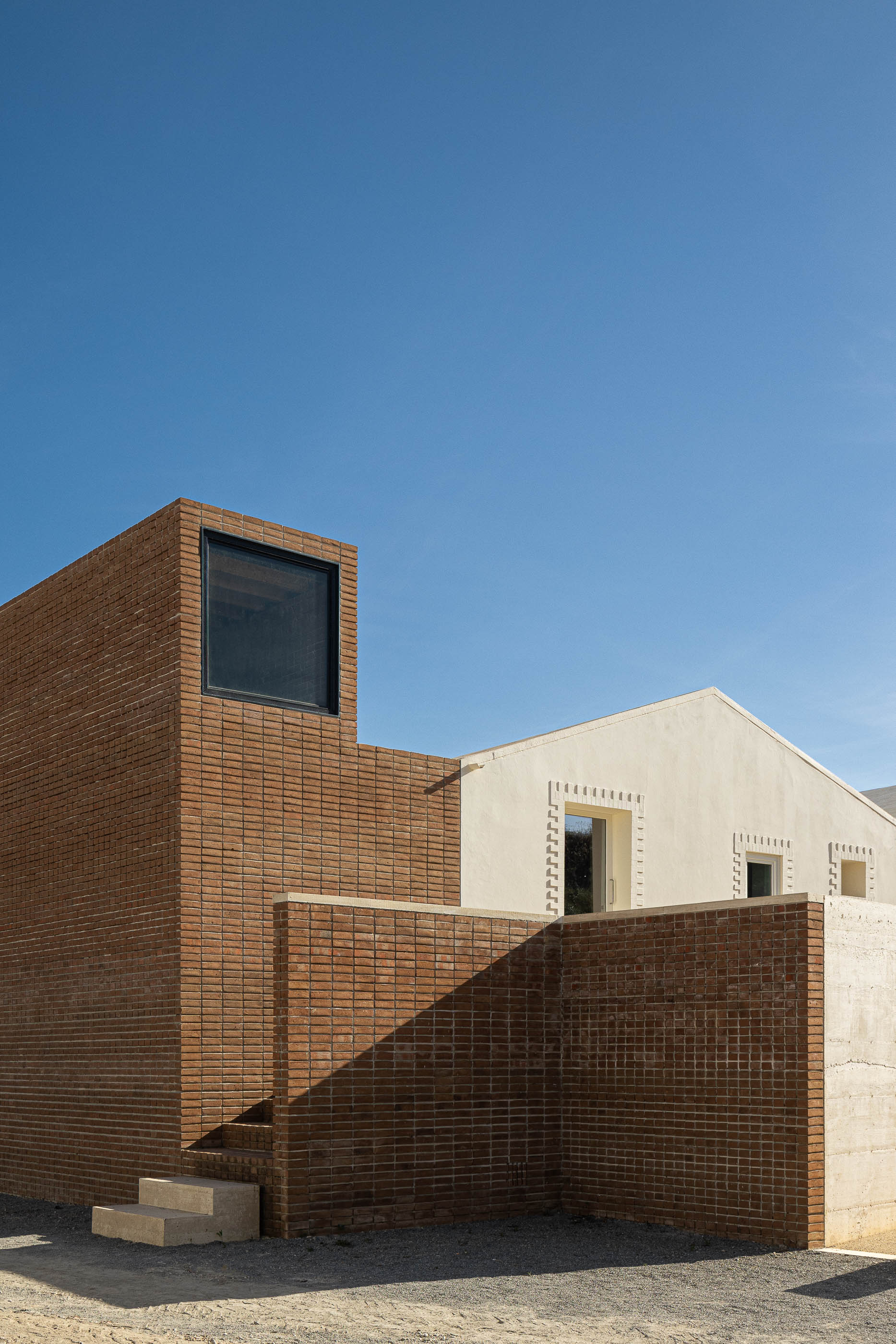 Fachada: Vista angular do edifício com torre de tijolo, paredes brancas e muro de betão. — Olaria Municipal arquitetura ARDE Arquitetura+Design em Odemira