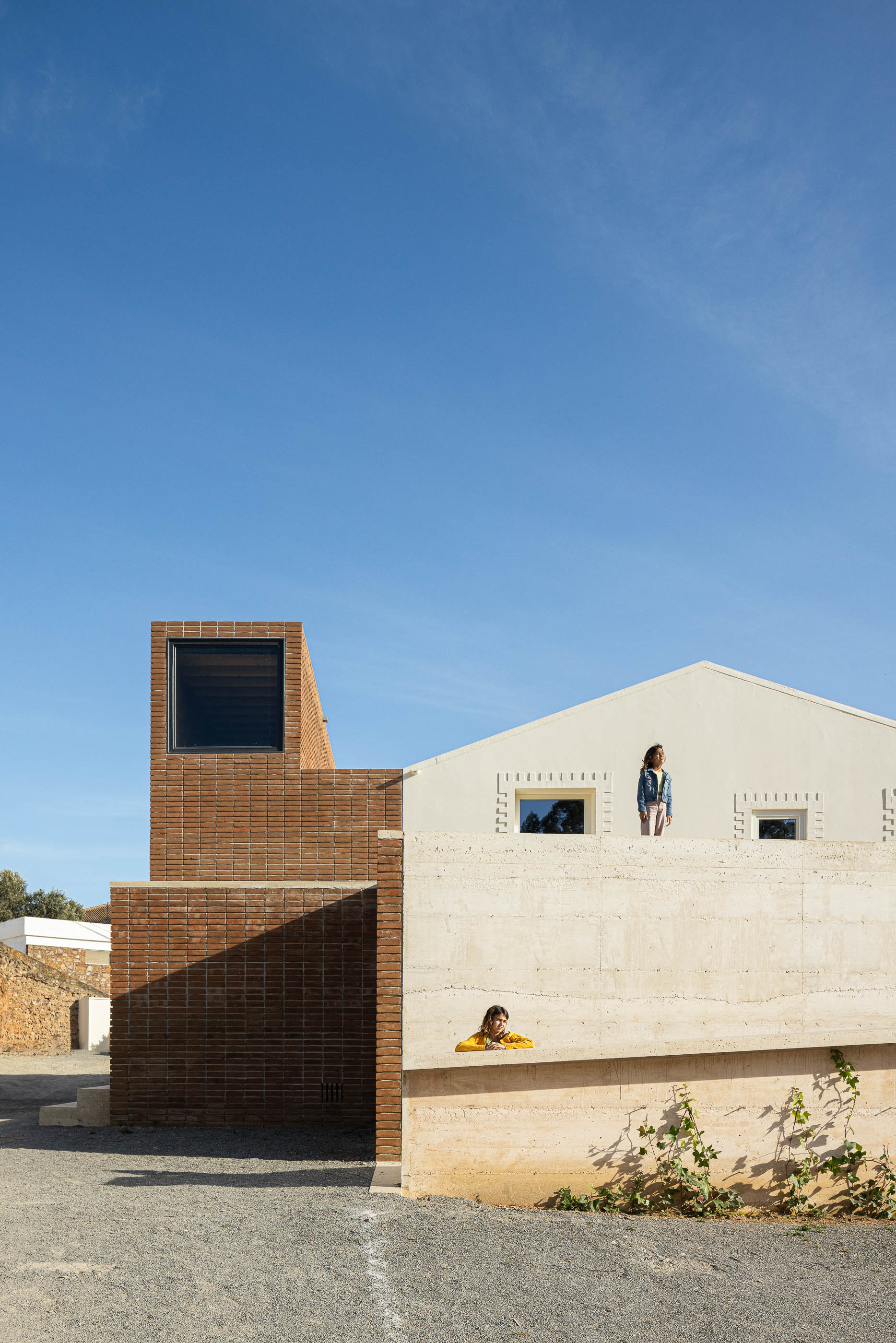 Exterior: Vista geral do edifício com torre de tijolo, paredes brancas e muro de betão. — Olaria Municipal arquitetura ARDE Arquitetura+Design em Odemira