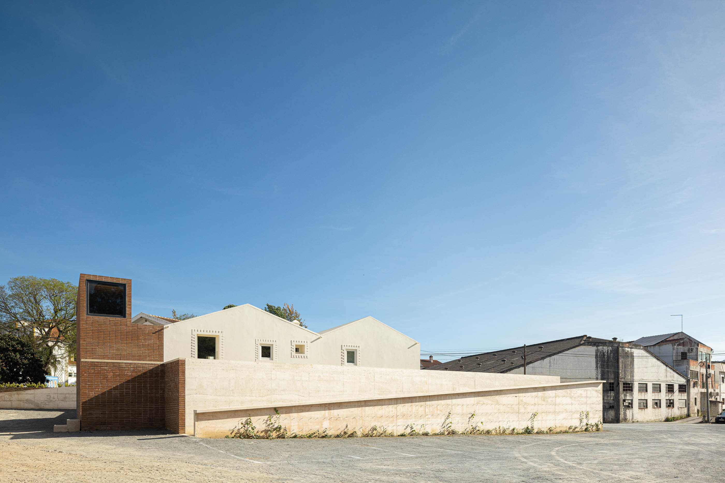 Exterior: Vista lateral do edifício com torre de tijolo, paredes brancas e muro de betão. — Olaria Municipal arquitetura ARDE Arquitetura+Design em Odemira