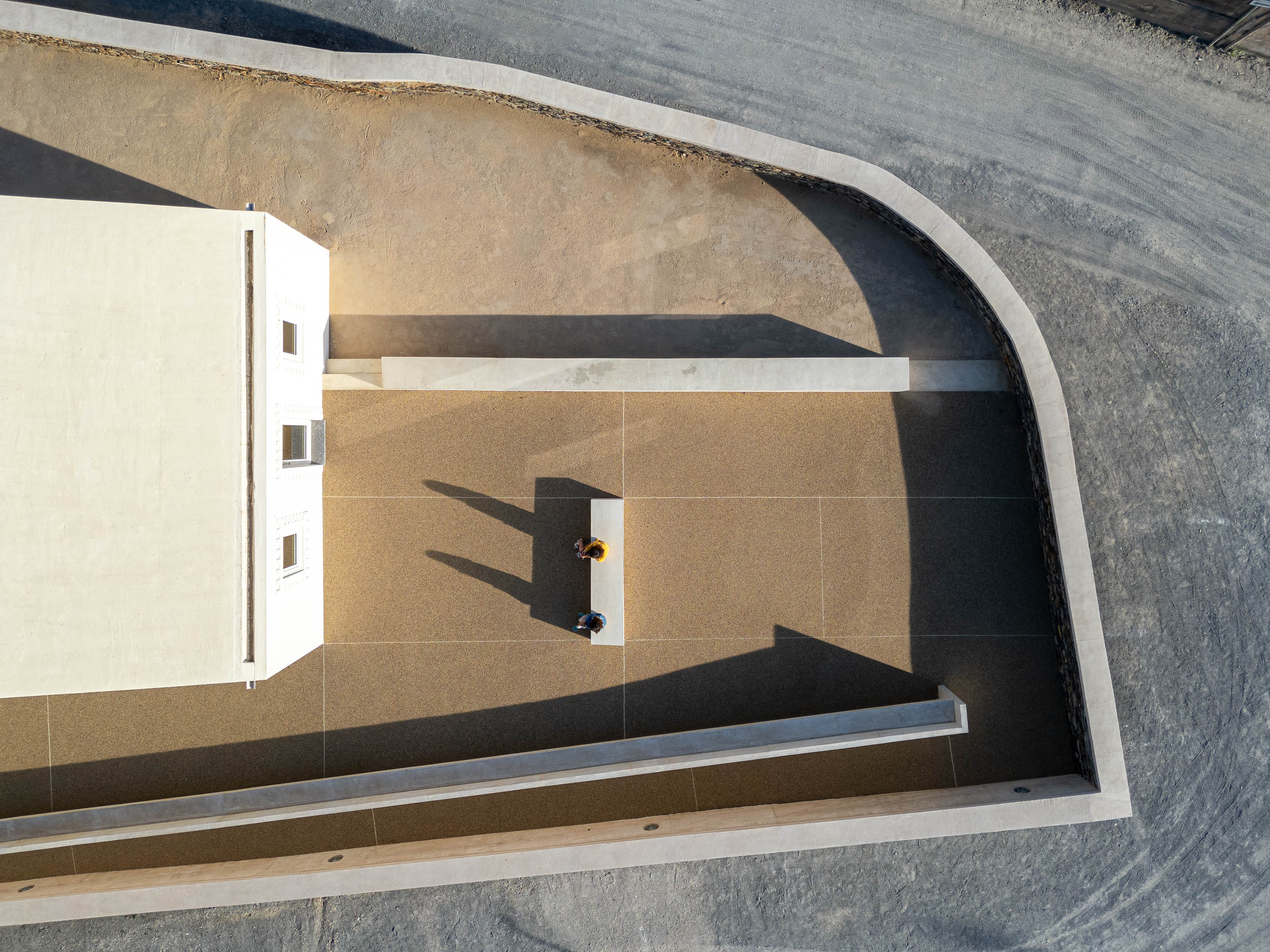 Exterior: Vista de cima do pátio com pavimento de gravilha, edifício branco e muro de betão. — Olaria Municipal arquitetura ARDE Arquitetura+Design em Odemira