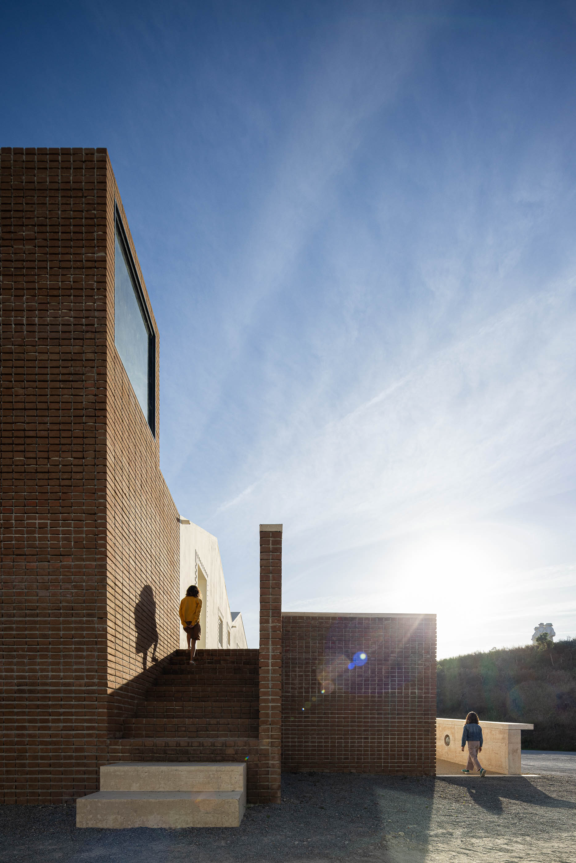 Escadaria exterior: Pessoas a subir escadas de tijolo, com torre de tijolo ao fundo. — Olaria Municipal arquitetura ARDE Arquitetura+Design em Odemira