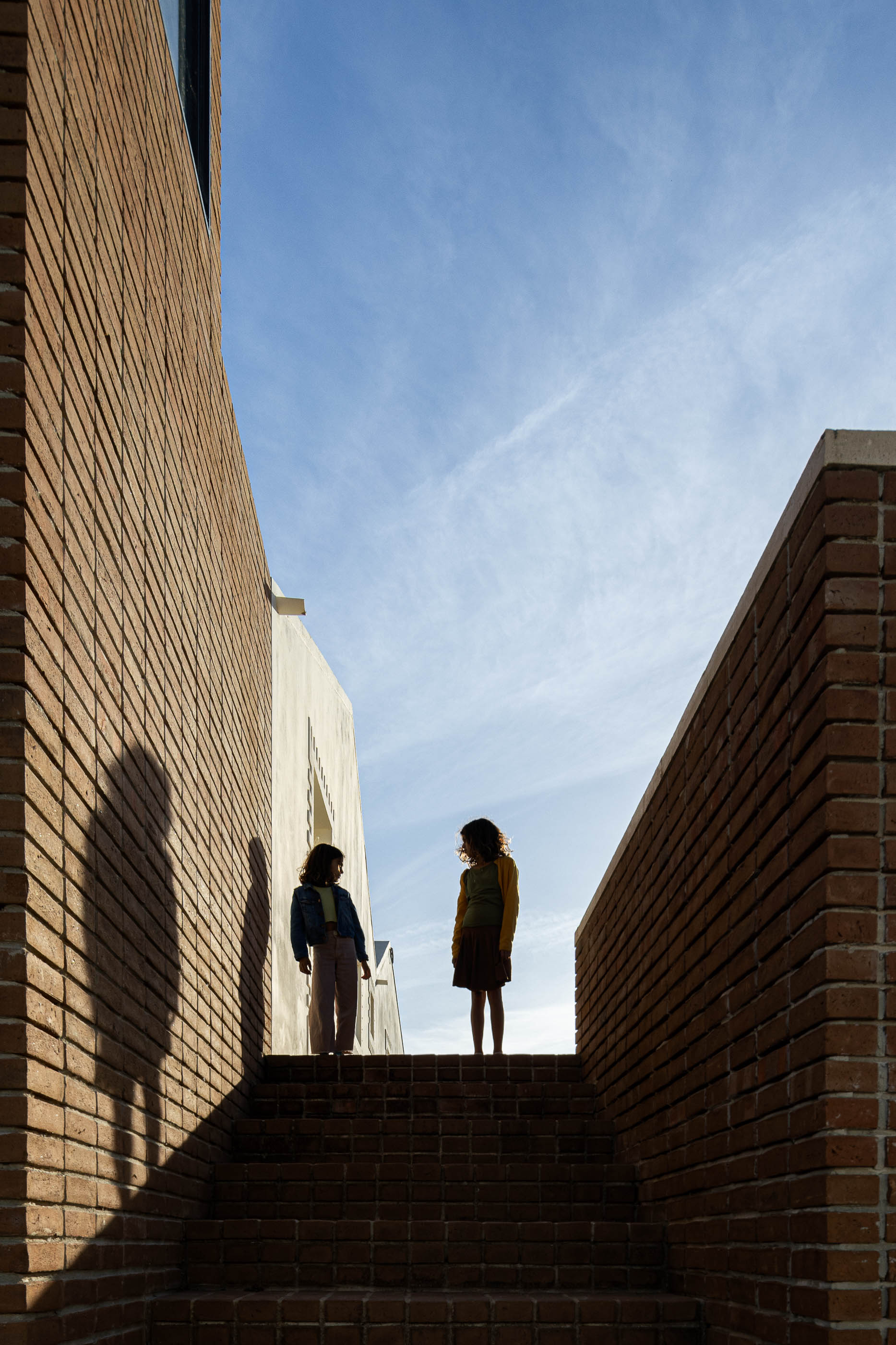 Escadaria exterior: Pessoas a conversar nas escadas de tijolo, com paredes de tijolo adjacentes. — Olaria Municipal arquitetura ARDE Arquitetura+Design em Odemira