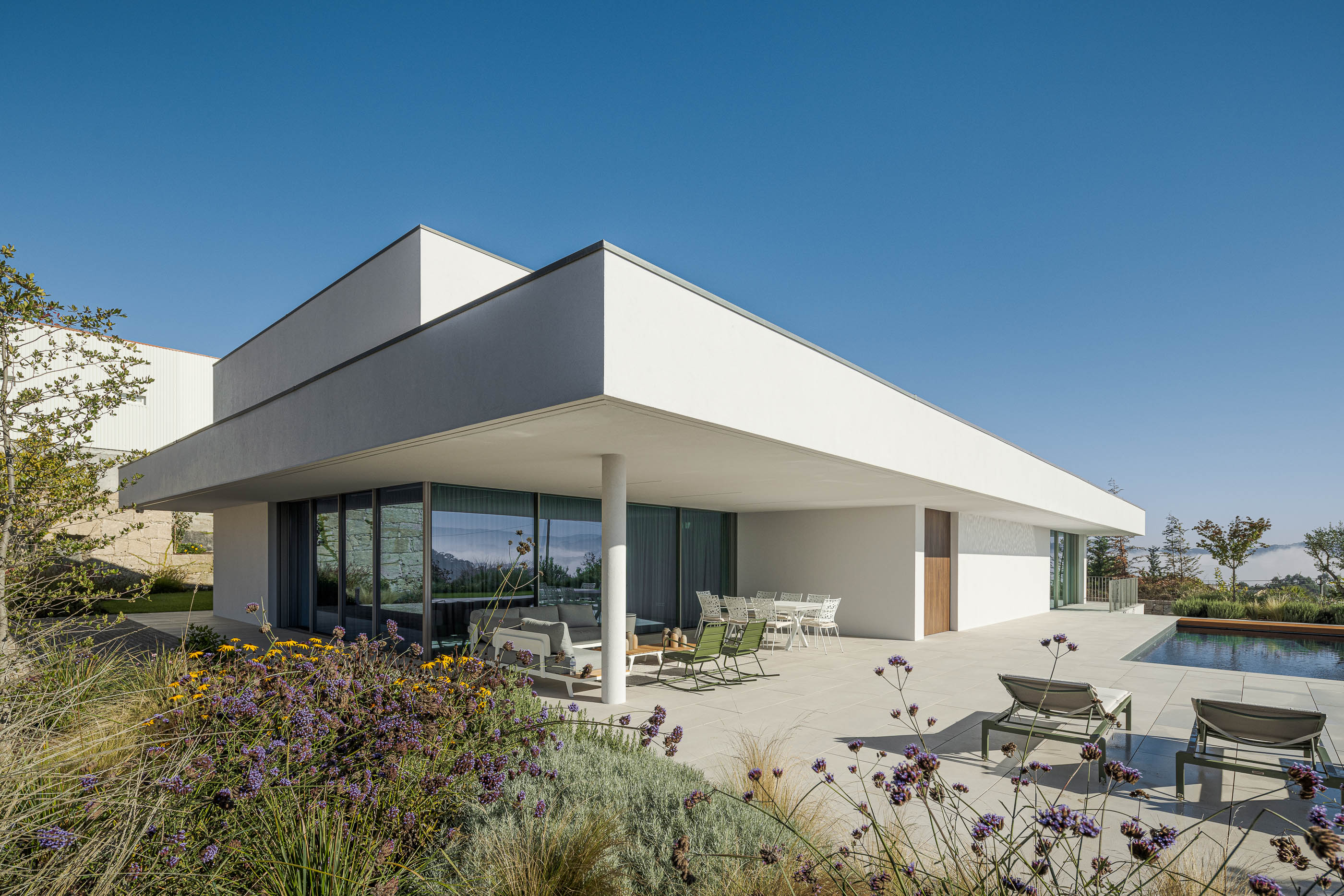 Exterior da moradia com terraço coberto, piscina e paisagismo exuberante. Arquitetura minimalista branca. — Habitação Áurea arquitetura stu.dere em Amarante