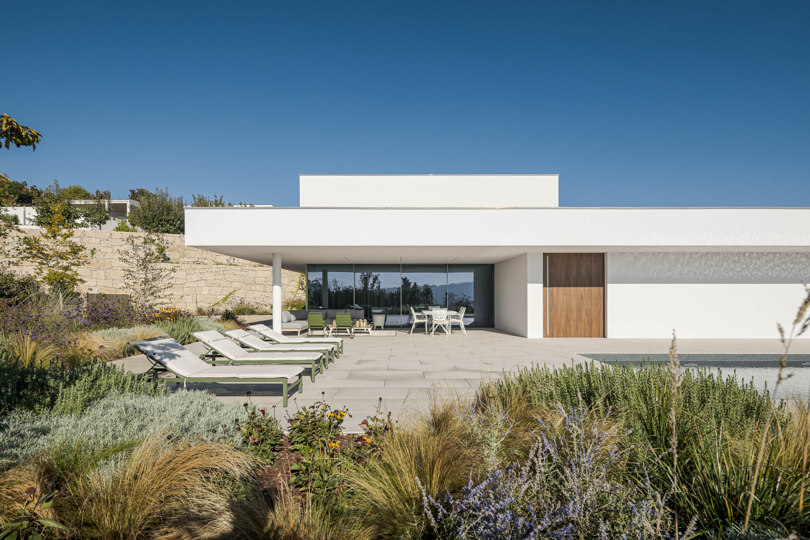 Exterior da moradia com piscina, espreguiçadeiras e jardim com vegetação diversa. — Habitação Áurea arquitetura stu.dere em Amarante