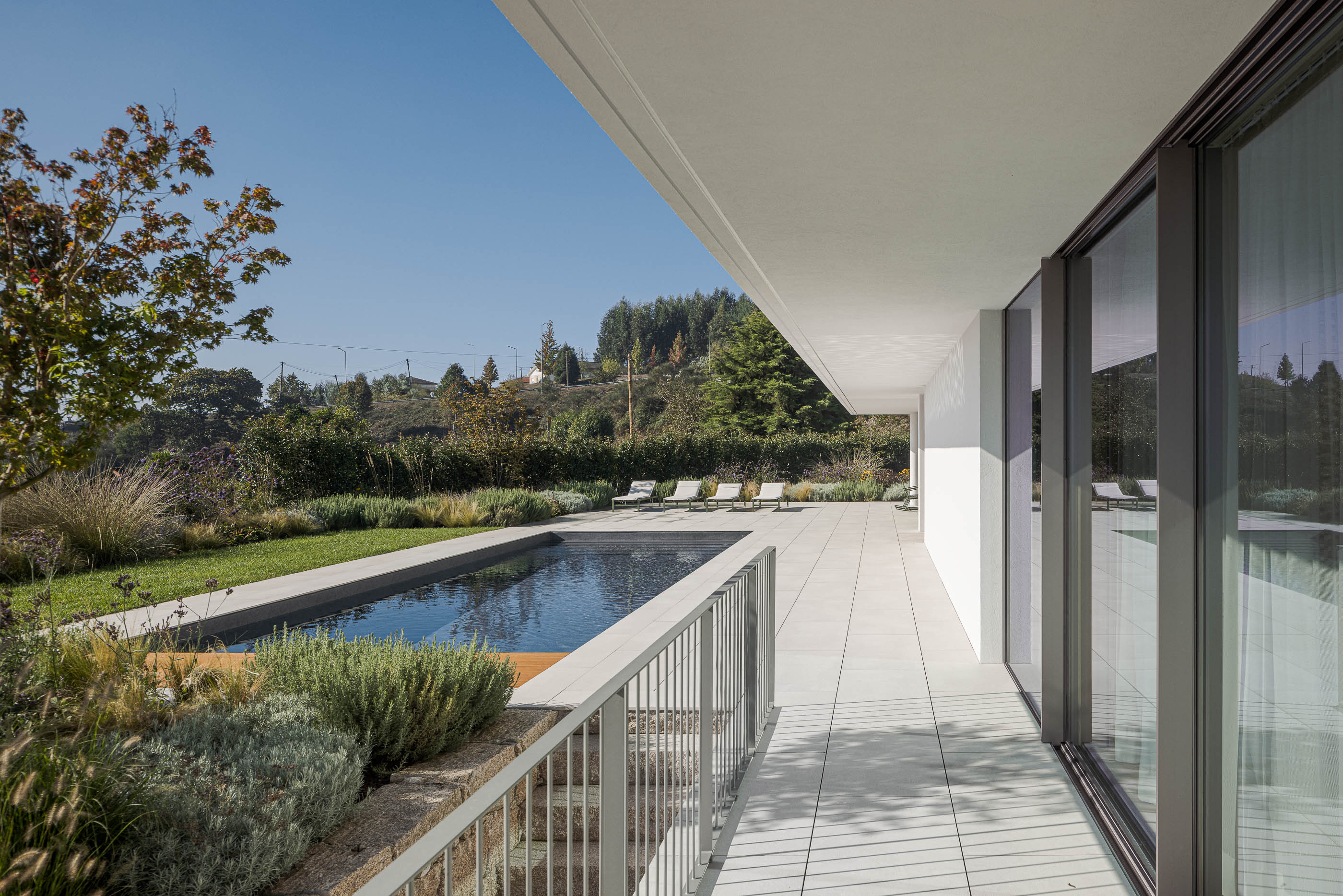 Exterior da moradia com piscina, relvado e janelas amplas refletindo a paisagem. — Habitação Áurea arquitetura stu.dere em Amarante