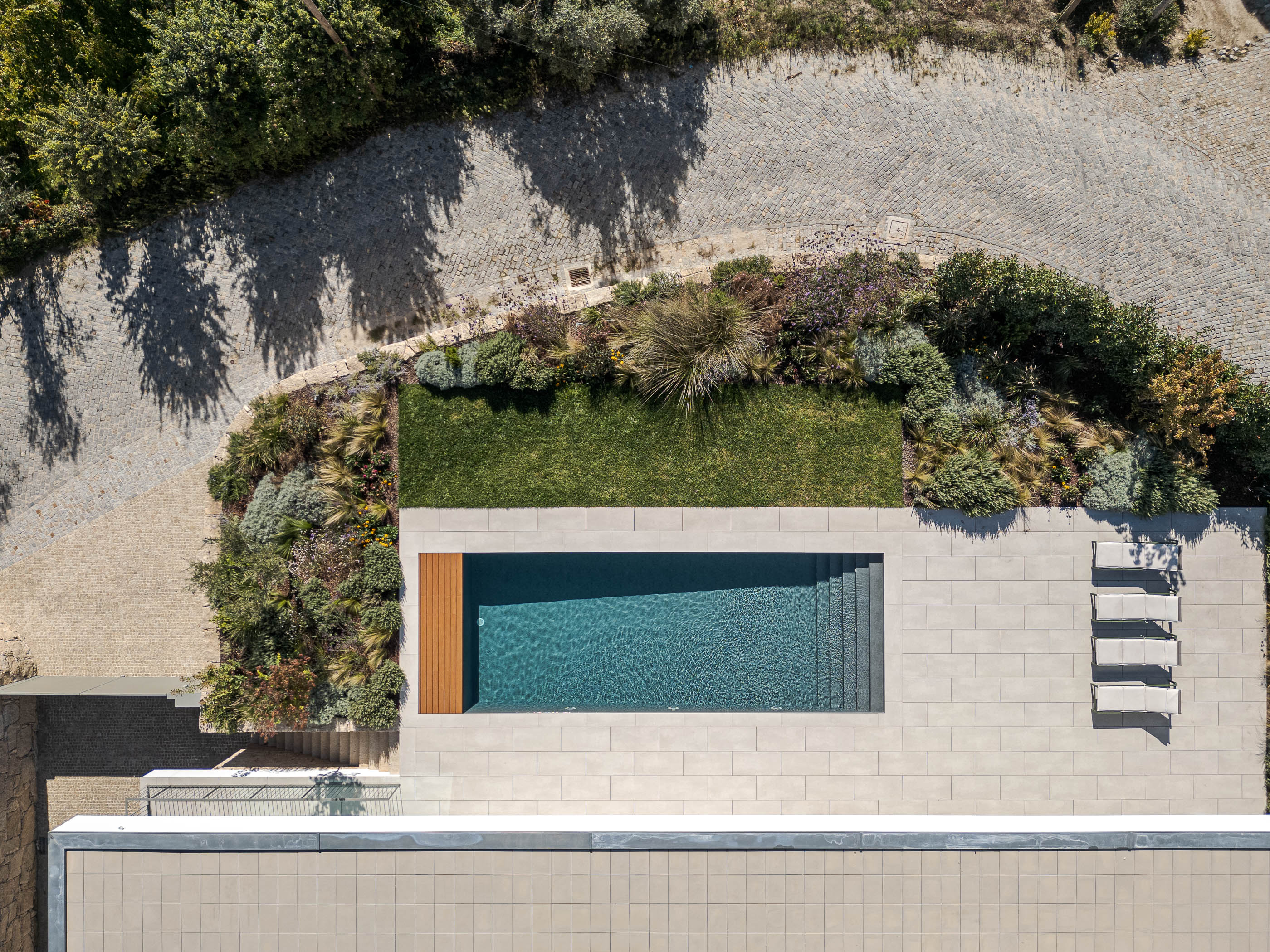 Vista aérea da piscina retangular com deck de madeira, rodeada por vegetação e pavimento cerâmico. — Habitação Áurea arquitetura stu.dere em Amarante