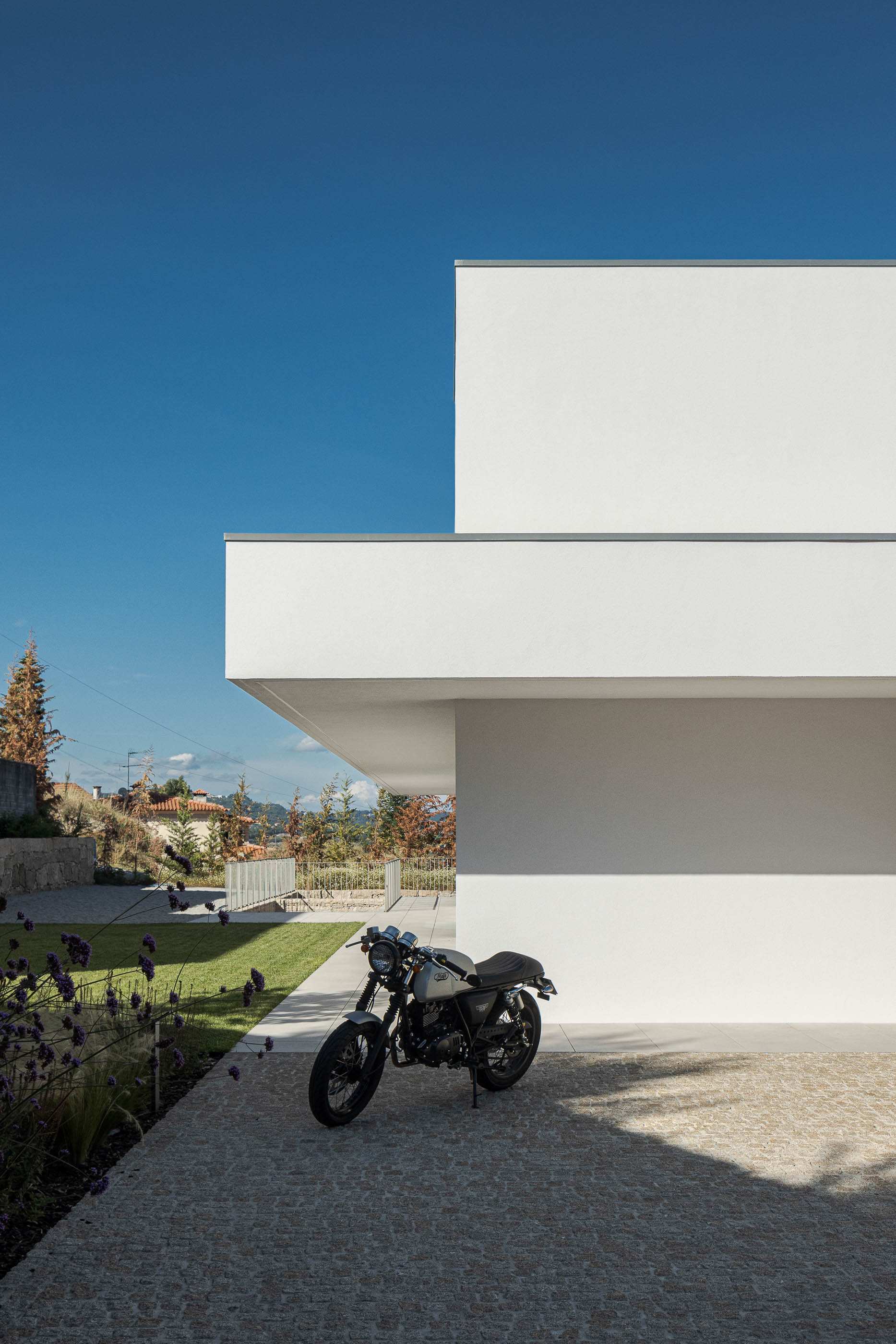 Exterior da moradia com mota estacionada em calçada portuguesa. Arquitetura minimalista branca. — Habitação Áurea arquitetura stu.dere em Amarante