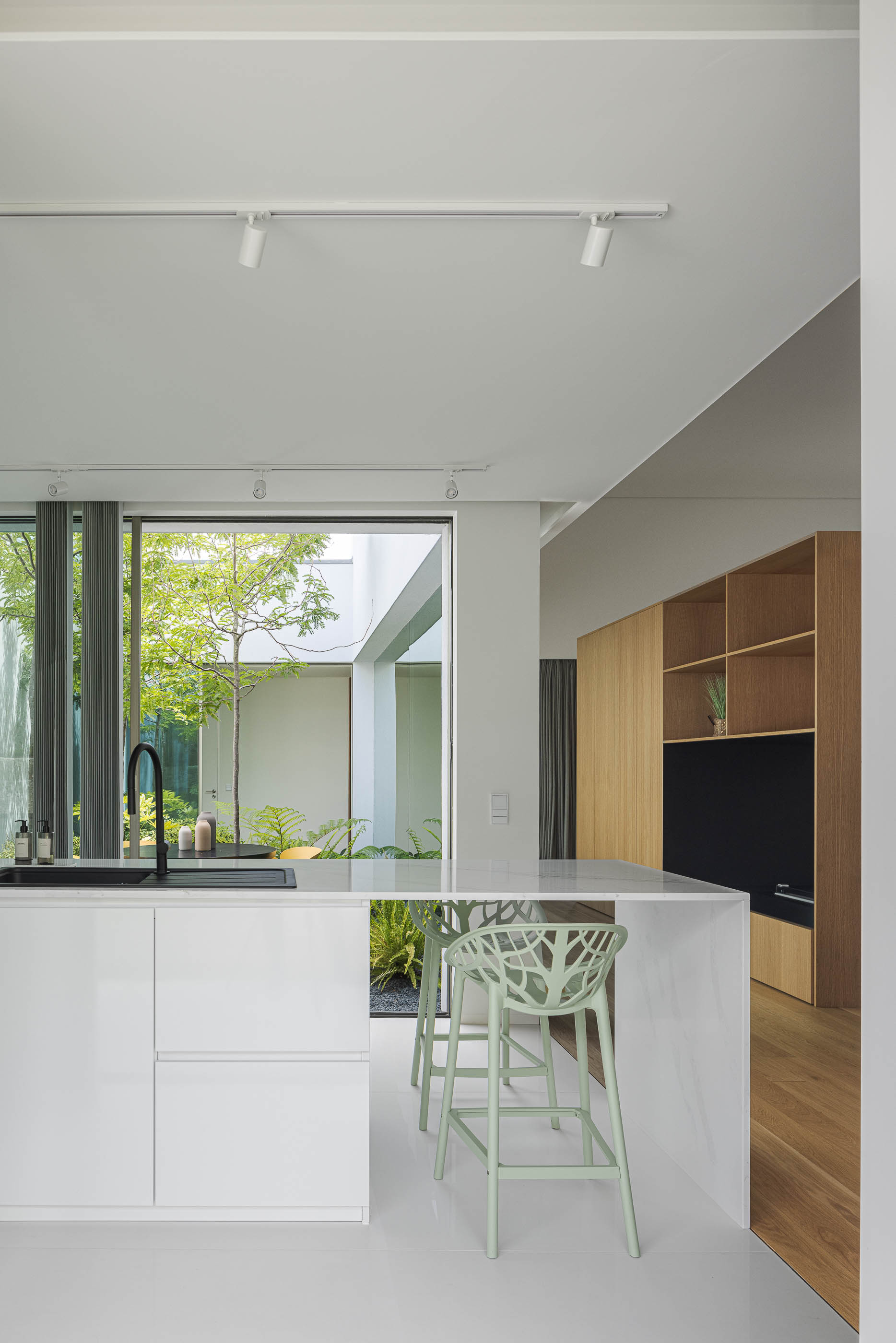 Cozinha com ilha central em branco e cadeiras verdes. Vista para pátio interior. — Habitação Áurea arquitetura stu.dere em Amarante