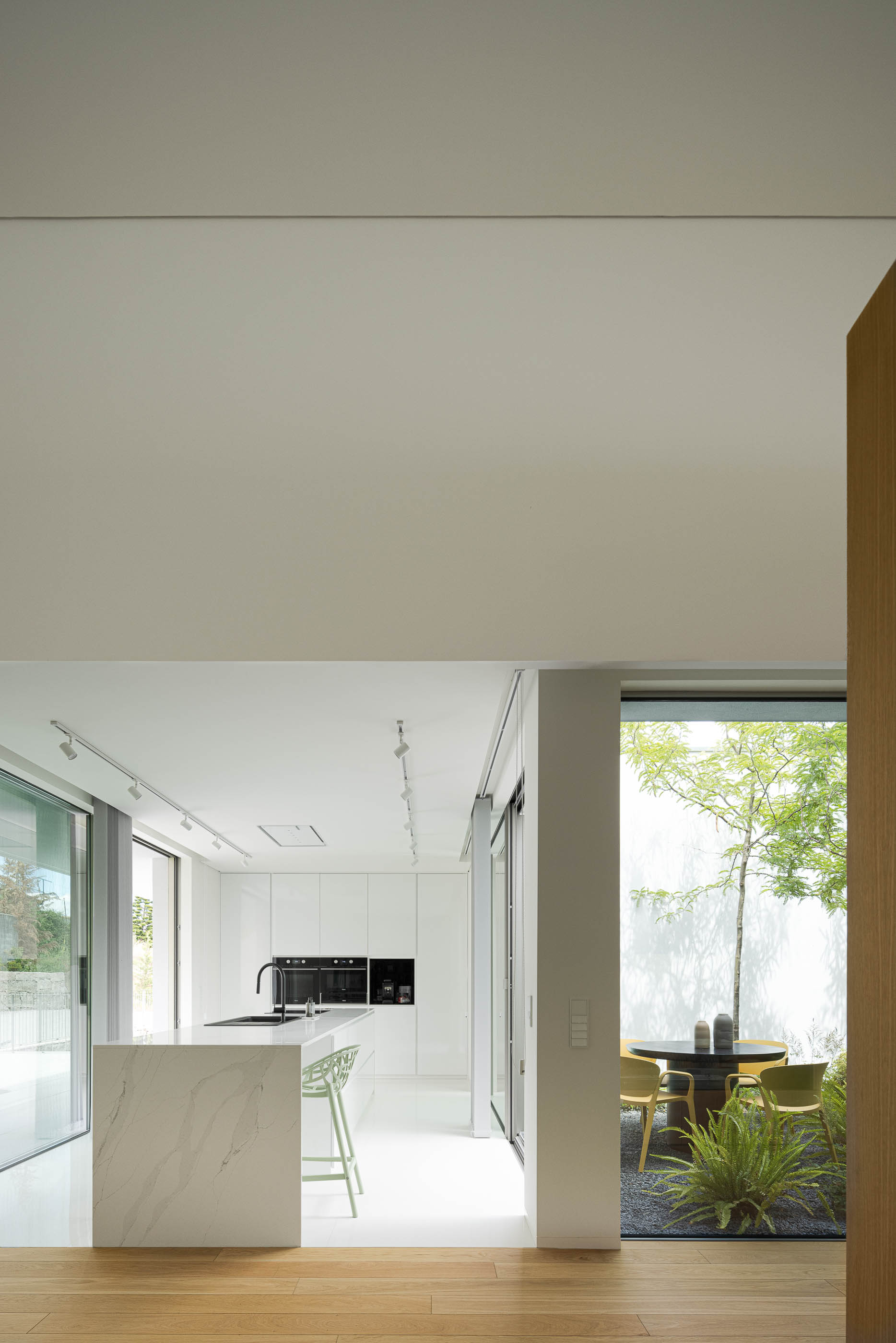 Cozinha minimalista com ilha central, pavimento cerâmico e vista para pátio interior. — Habitação Áurea arquitetura stu.dere em Amarante