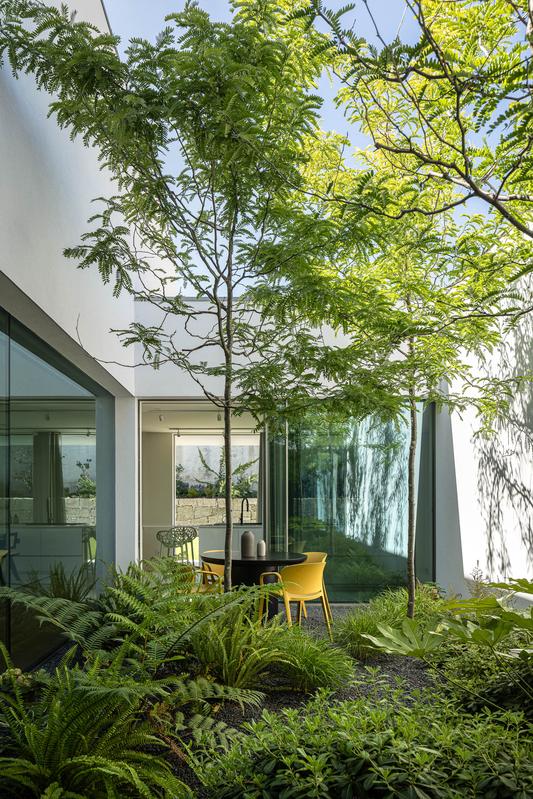 Pátio interior com mesa redonda, cadeiras amarelas e vegetação exuberante. — Habitação Áurea arquitetura stu.dere em Amarante
