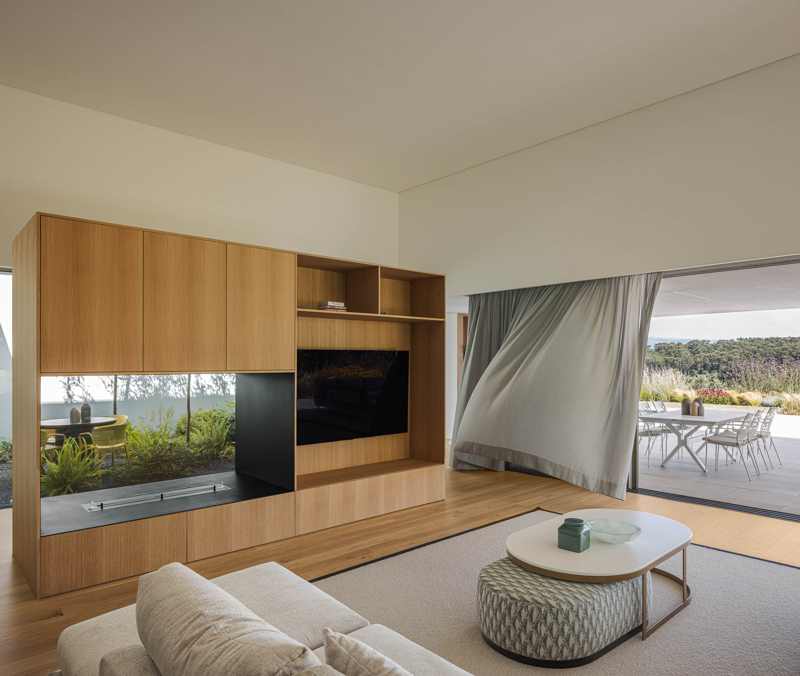 Sala de estar com móvel de madeira embutido, sofá bege e alcatifa clara. — Habitação Áurea arquitetura stu.dere em Amarante
