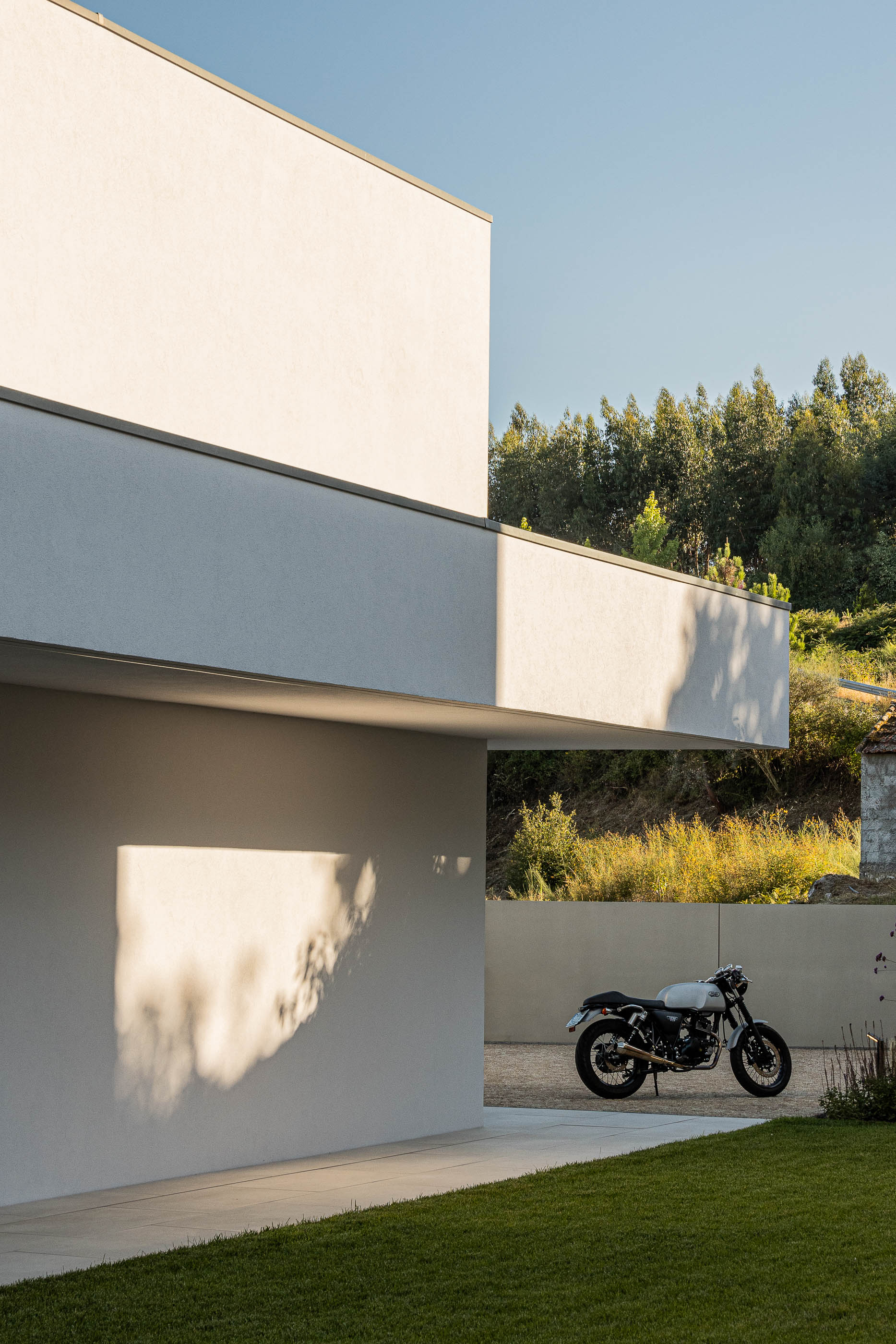 Exterior da moradia com mota estacionada e relvado. Arquitetura minimalista branca. — Habitação Áurea arquitetura stu.dere em Amarante