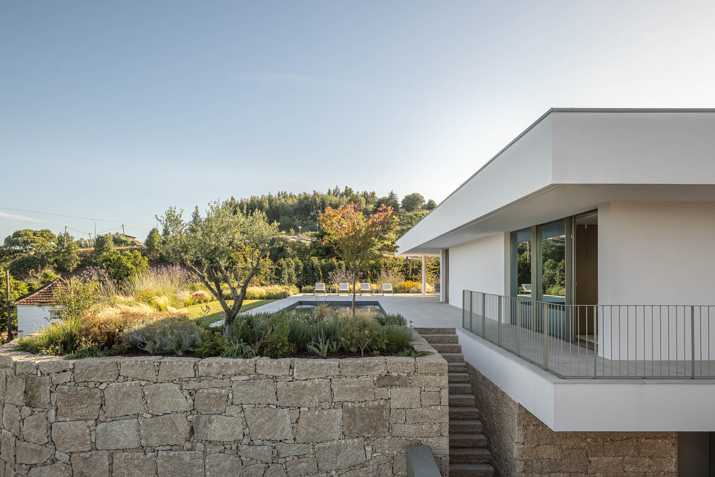 Exterior da moradia com piscina, jardim e muro de pedra. — Habitação Áurea arquitetura stu.dere em Amarante