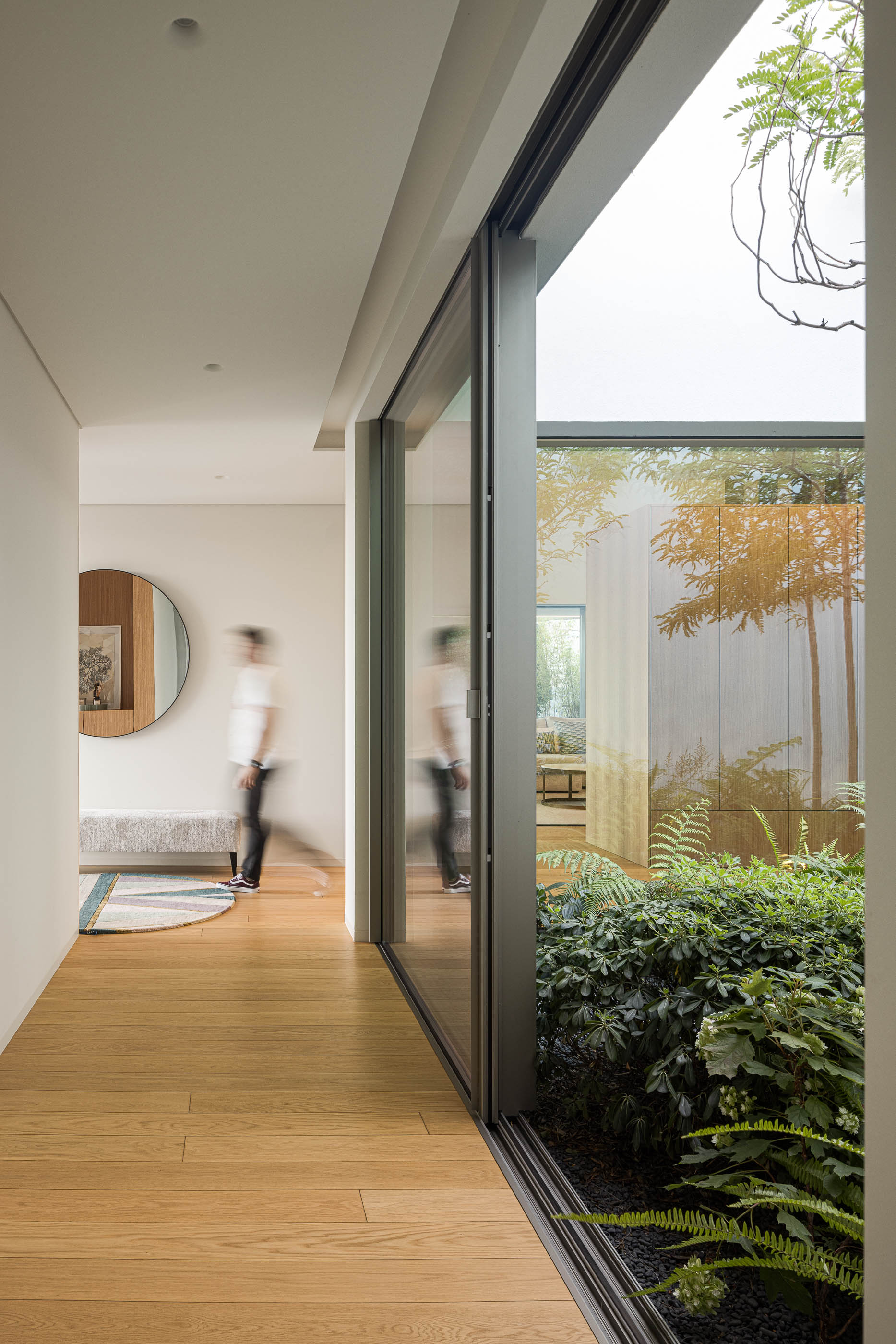 Corredor com pavimento de madeira e vista para pátio interior com vegetação. — Habitação Áurea arquitetura stu.dere em Amarante