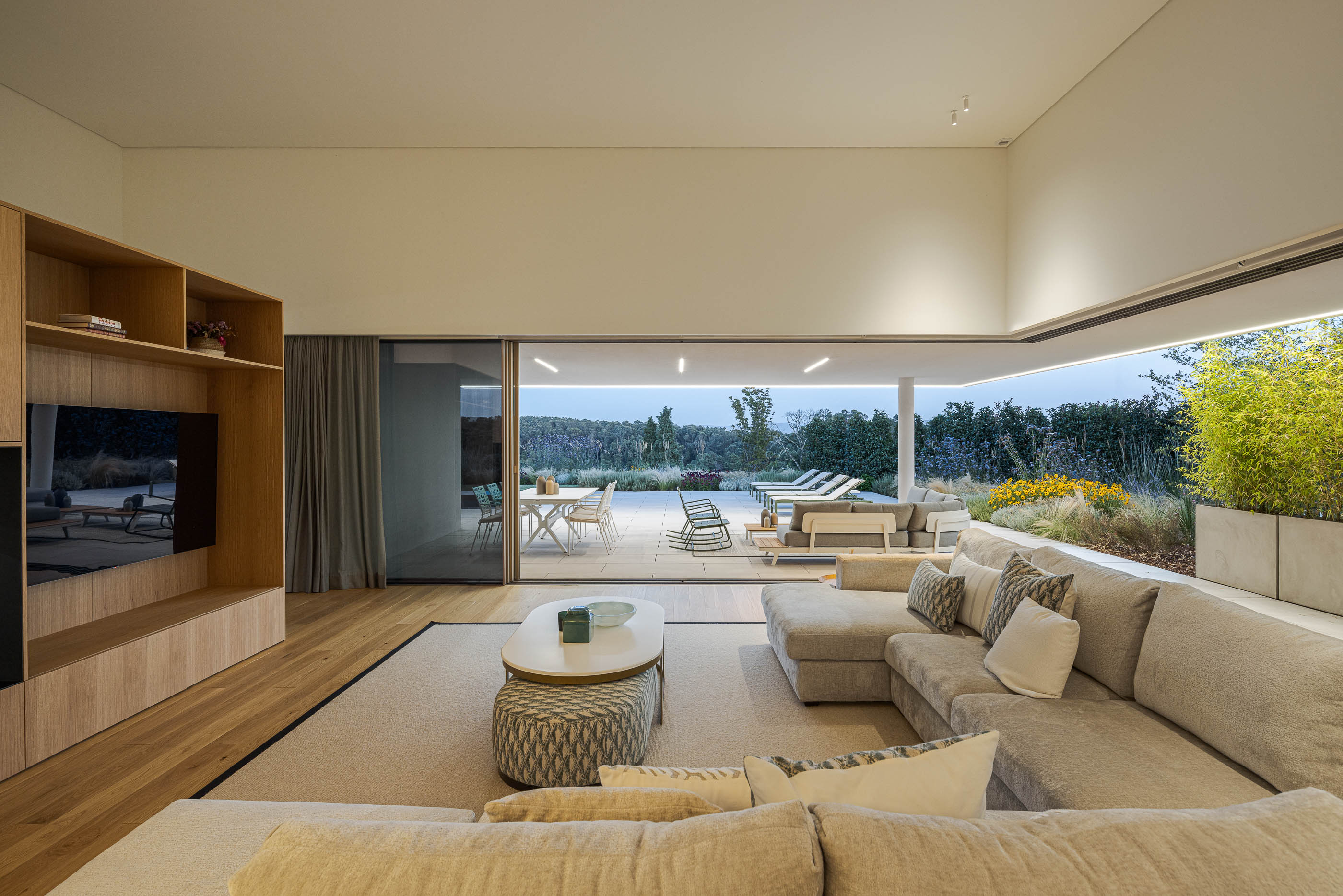 Sala de estar com sofá bege, móvel de madeira e vista para o terraço e piscina. — Habitação Áurea arquitetura stu.dere em Amarante
