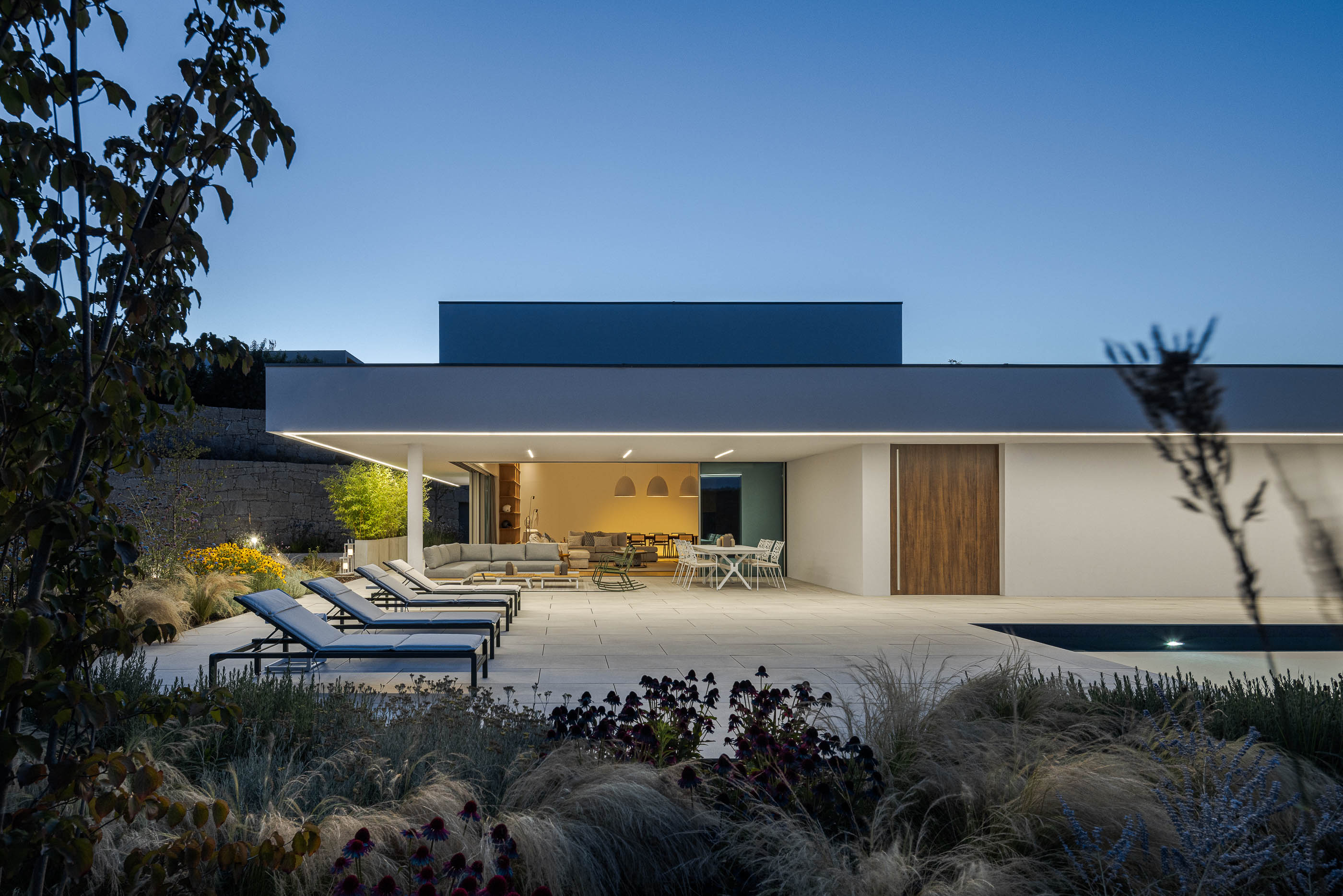 Exterior da moradia com terraço, piscina e jardim iluminado. — Habitação Áurea arquitetura stu.dere em Amarante