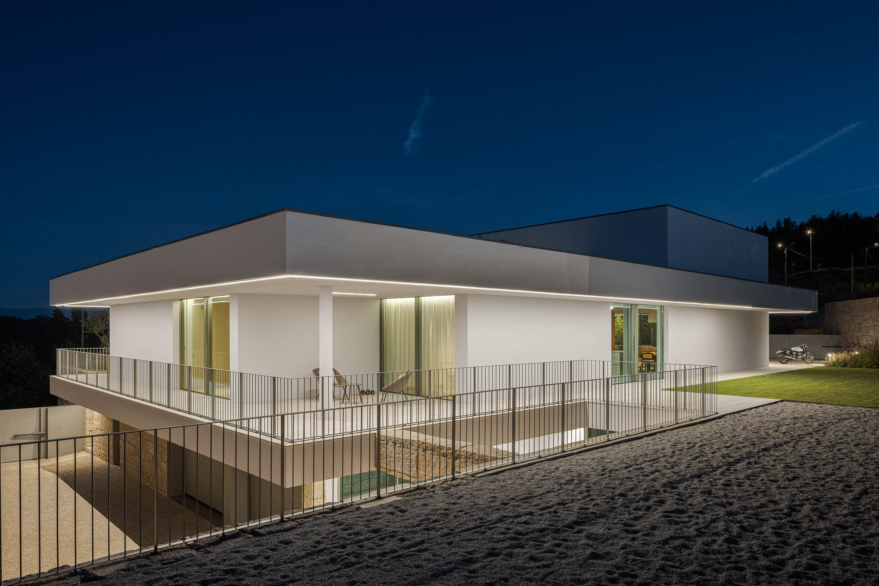 Exterior da moradia iluminada com varanda e garagem subterrânea. — Habitação Áurea arquitetura stu.dere em Amarante