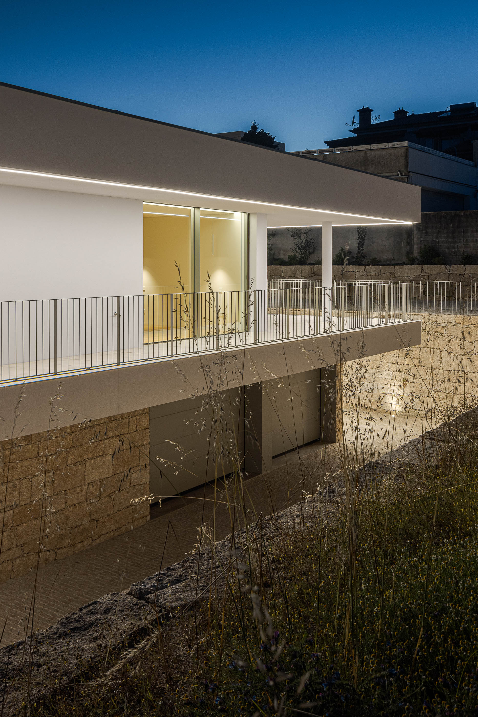 Exterior da moradia com garagem subterrânea e varanda iluminada. — Habitação Áurea arquitetura stu.dere em Amarante