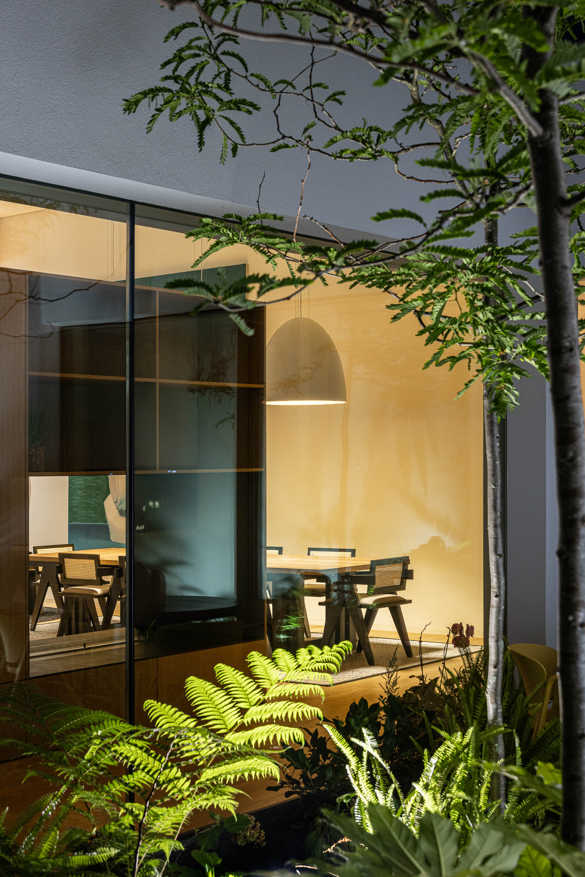 Sala de jantar com mesa de madeira e cadeiras, vista através do pátio interior. — Habitação Áurea arquitetura stu.dere em Amarante