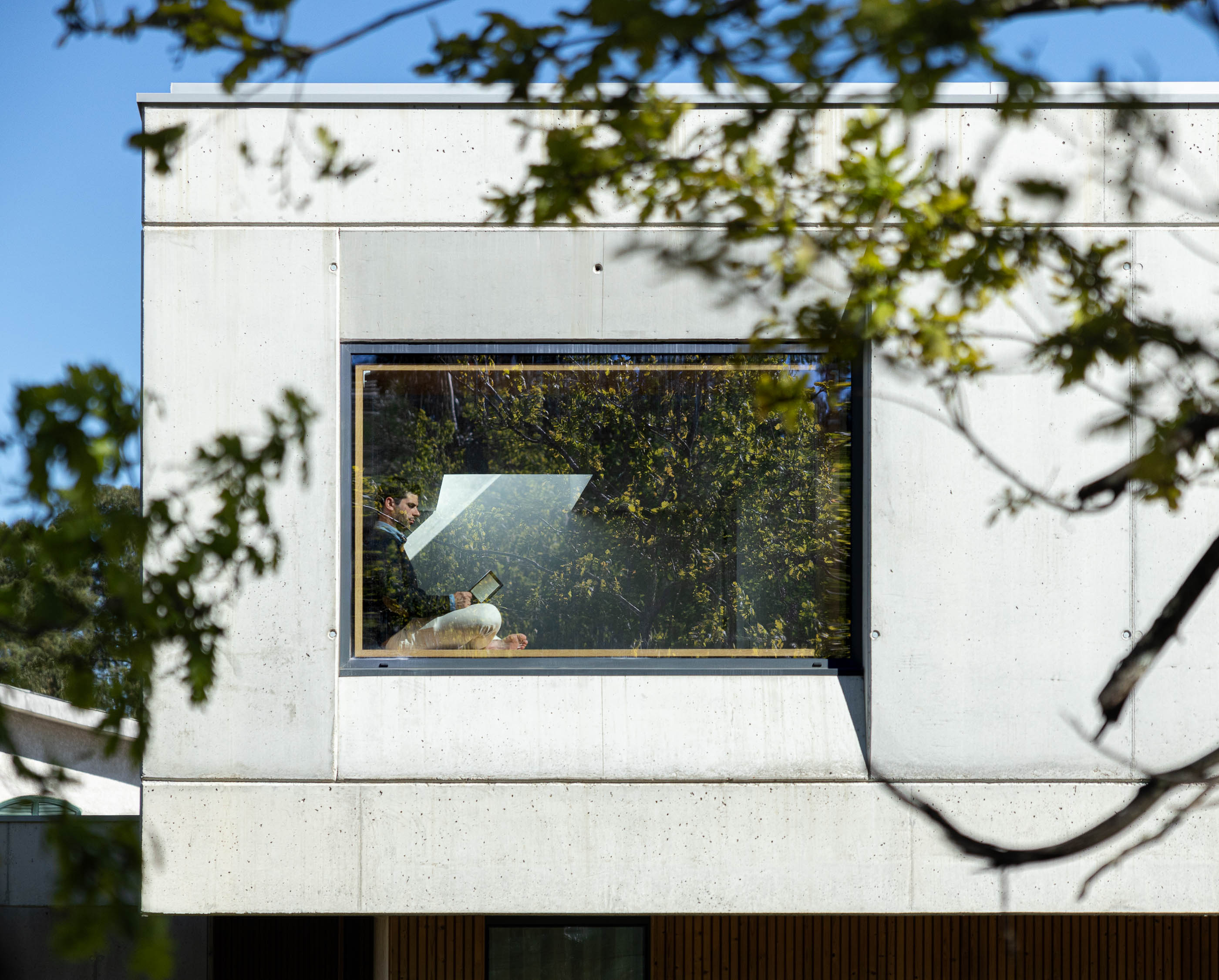 Quarto: Janela quadrada com moldura de madeira, homem sentado a ler com estantes embutidas. — Casa em Mundão arquitetura Um para Um, arquitectura e engenharia em Viseu
