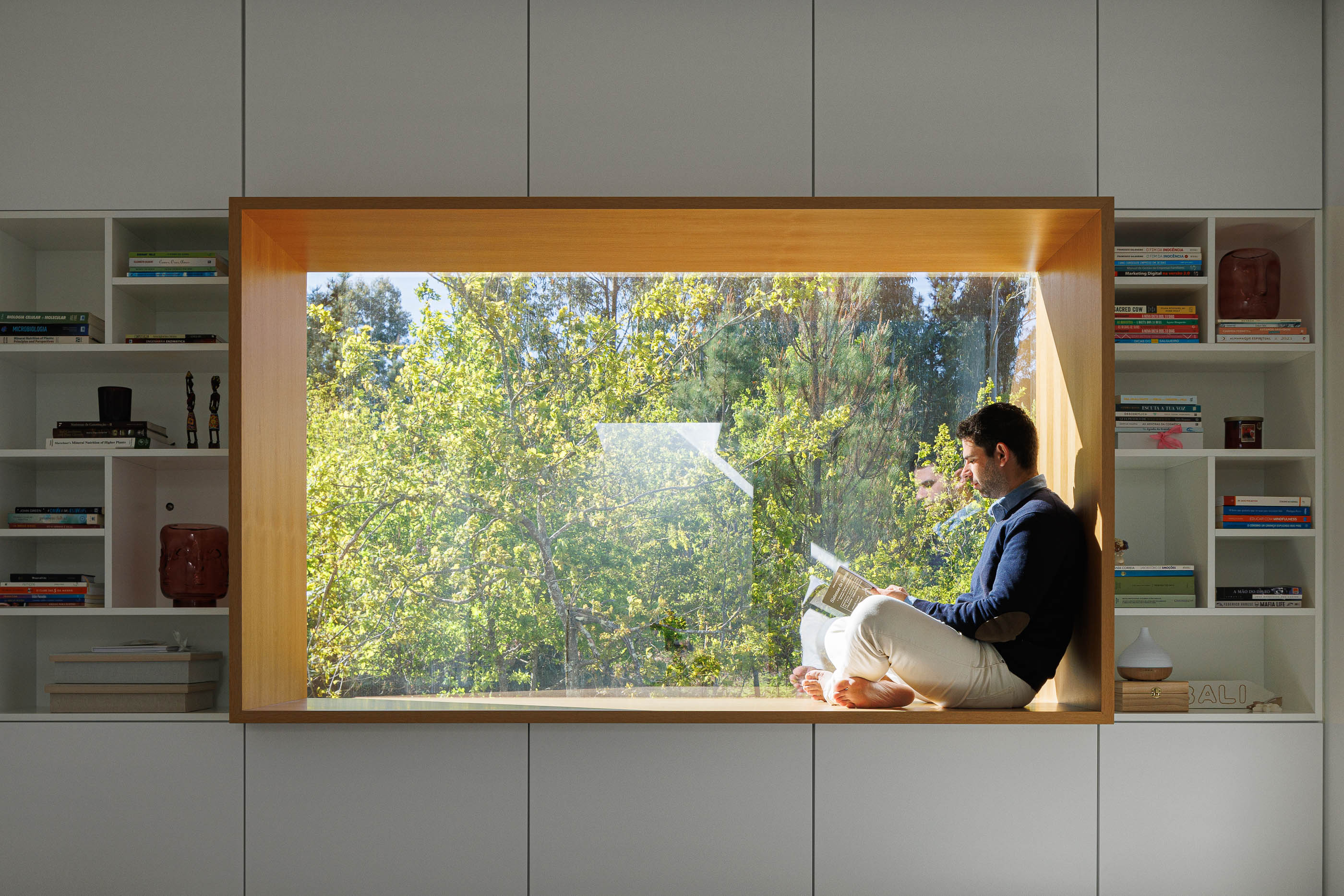 Quarto: Interior com janela embutida, estantes brancas e homem sentado a ler. — Casa em Mundão arquitetura Um para Um, arquitectura e engenharia em Viseu