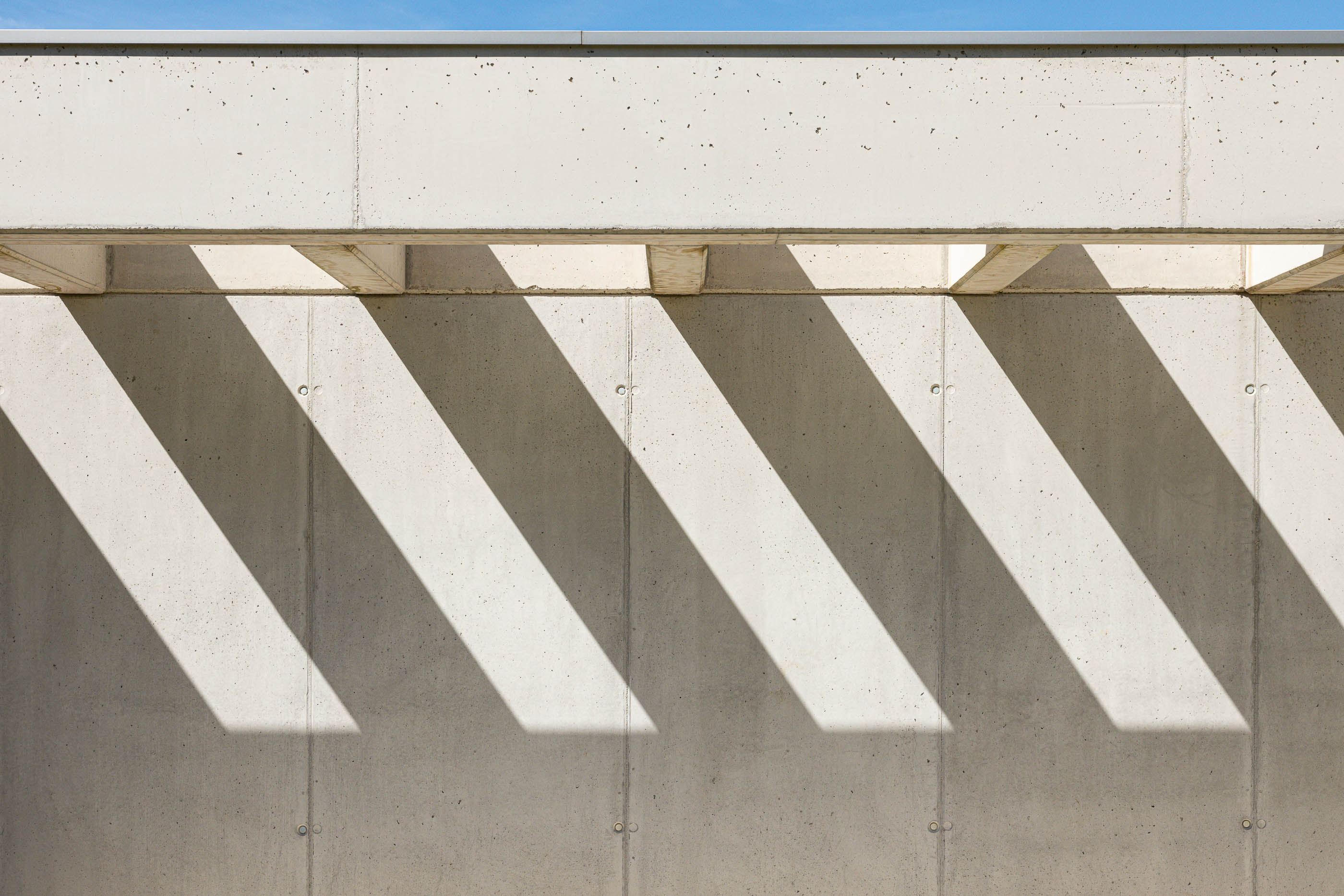 Exterior: Alpendre em betão com sombras geométricas projetadas na parede. — Casa em Mundão arquitetura Um para Um, arquitectura e engenharia em Viseu