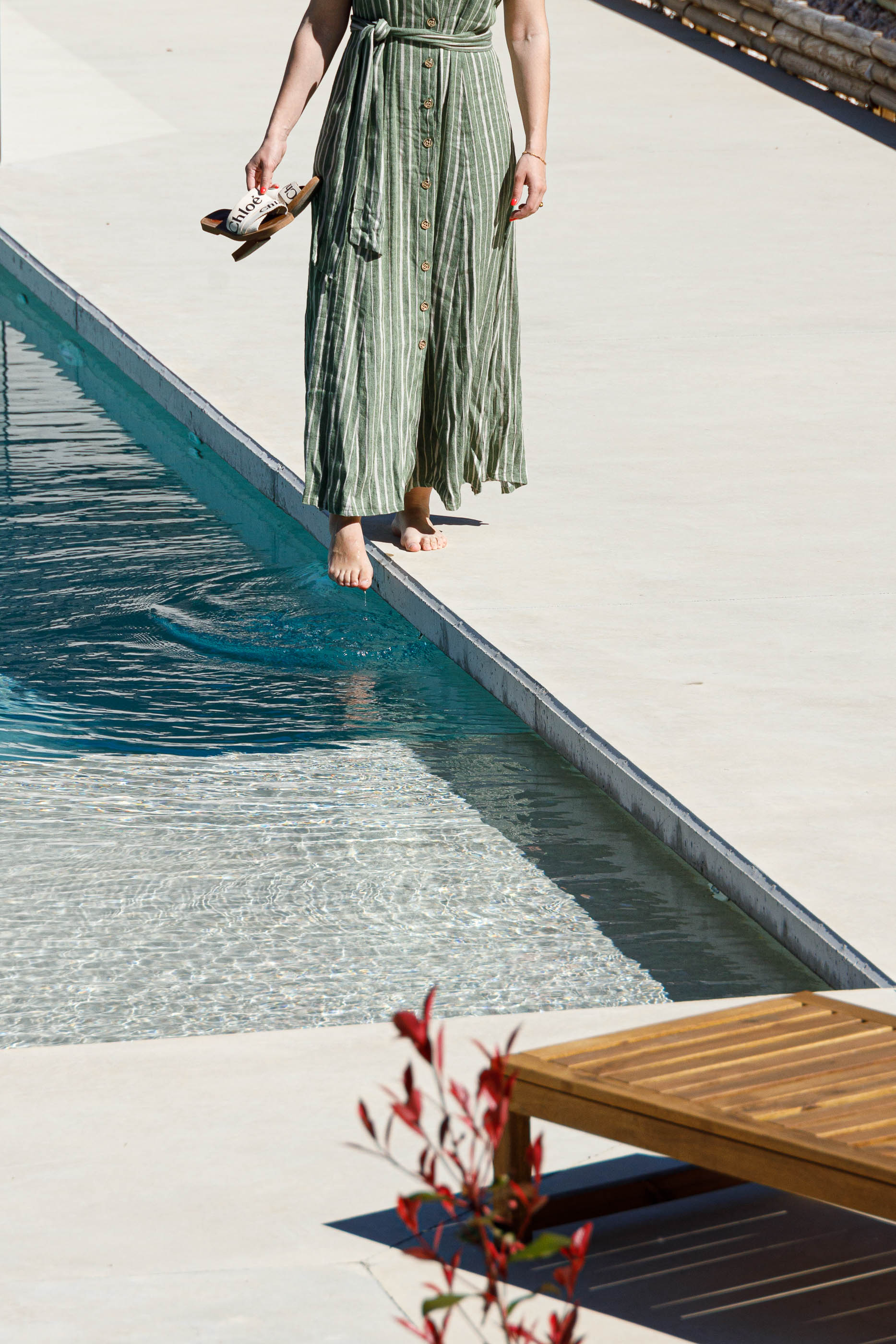 Exterior: Detalhe da piscina com mulher a tocar na água e espreguiçadeira de madeira. — Casa em Mundão arquitetura Um para Um, arquitectura e engenharia em Viseu