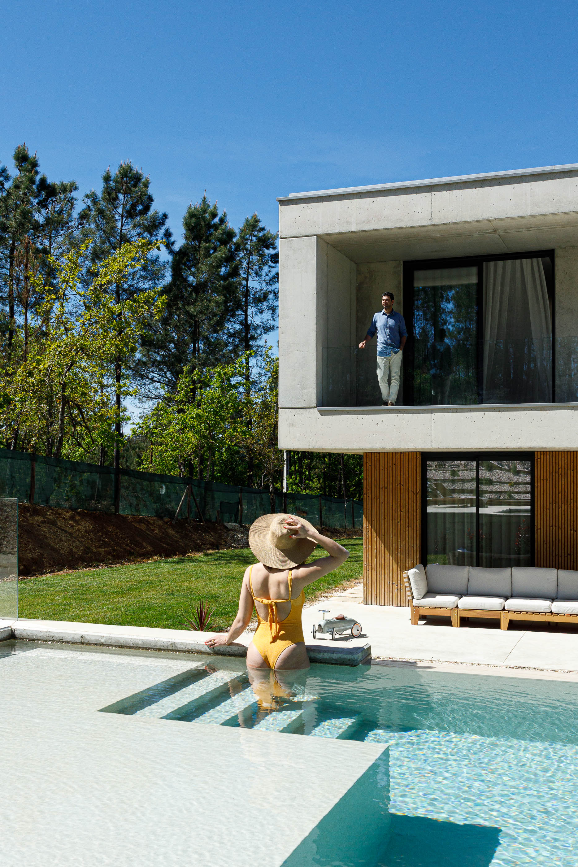 Exterior: Piscina com mulher a entrar na água e varanda em betão no andar superior. — Casa em Mundão arquitetura Um para Um, arquitectura e engenharia em Viseu