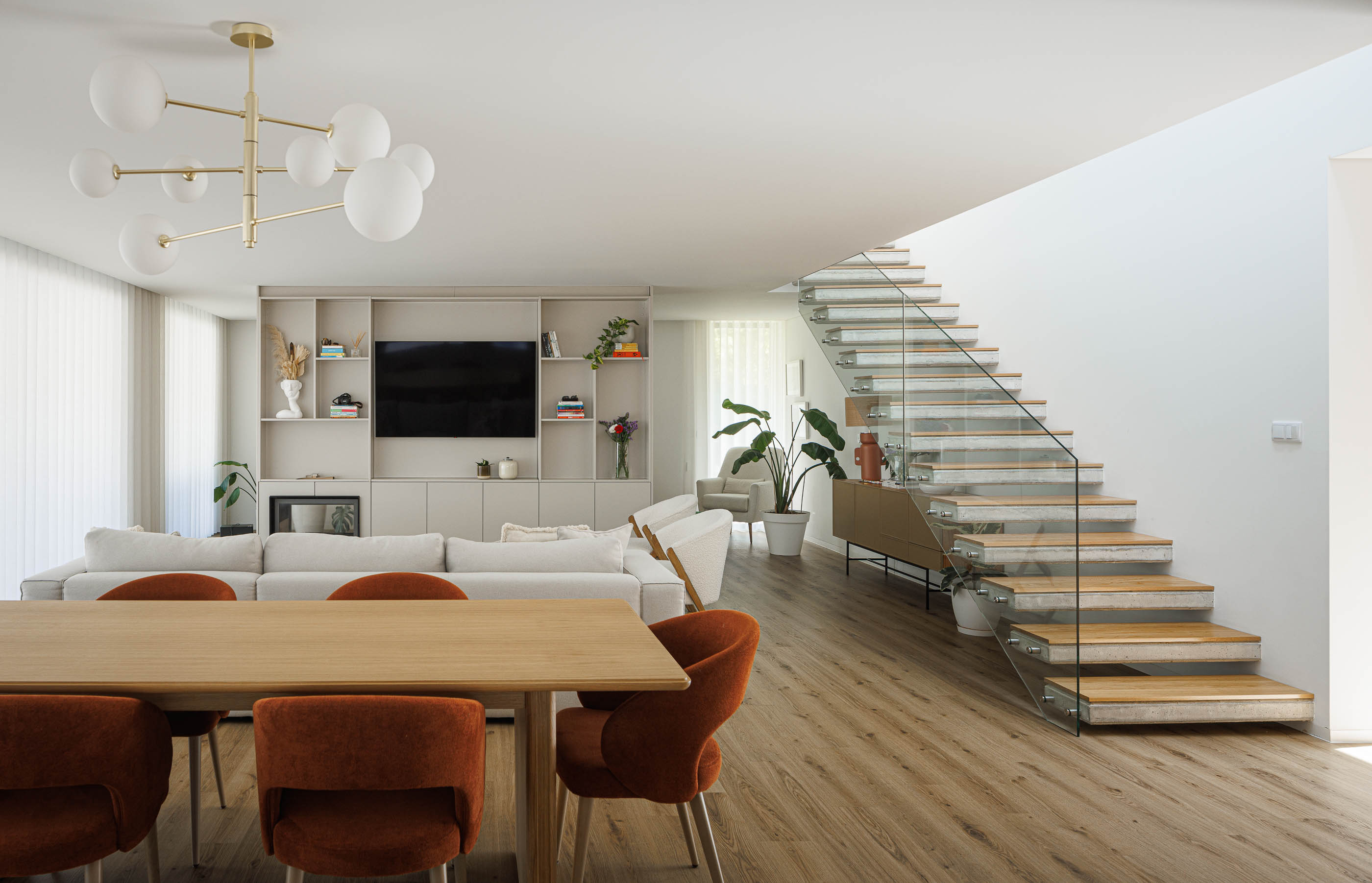 Sala de estar/Jantar: Espaço amplo com mesa de jantar, cadeiras, sofá e escadas com vidro. — Casa em Mundão arquitetura Um para Um, arquitectura e engenharia em Viseu