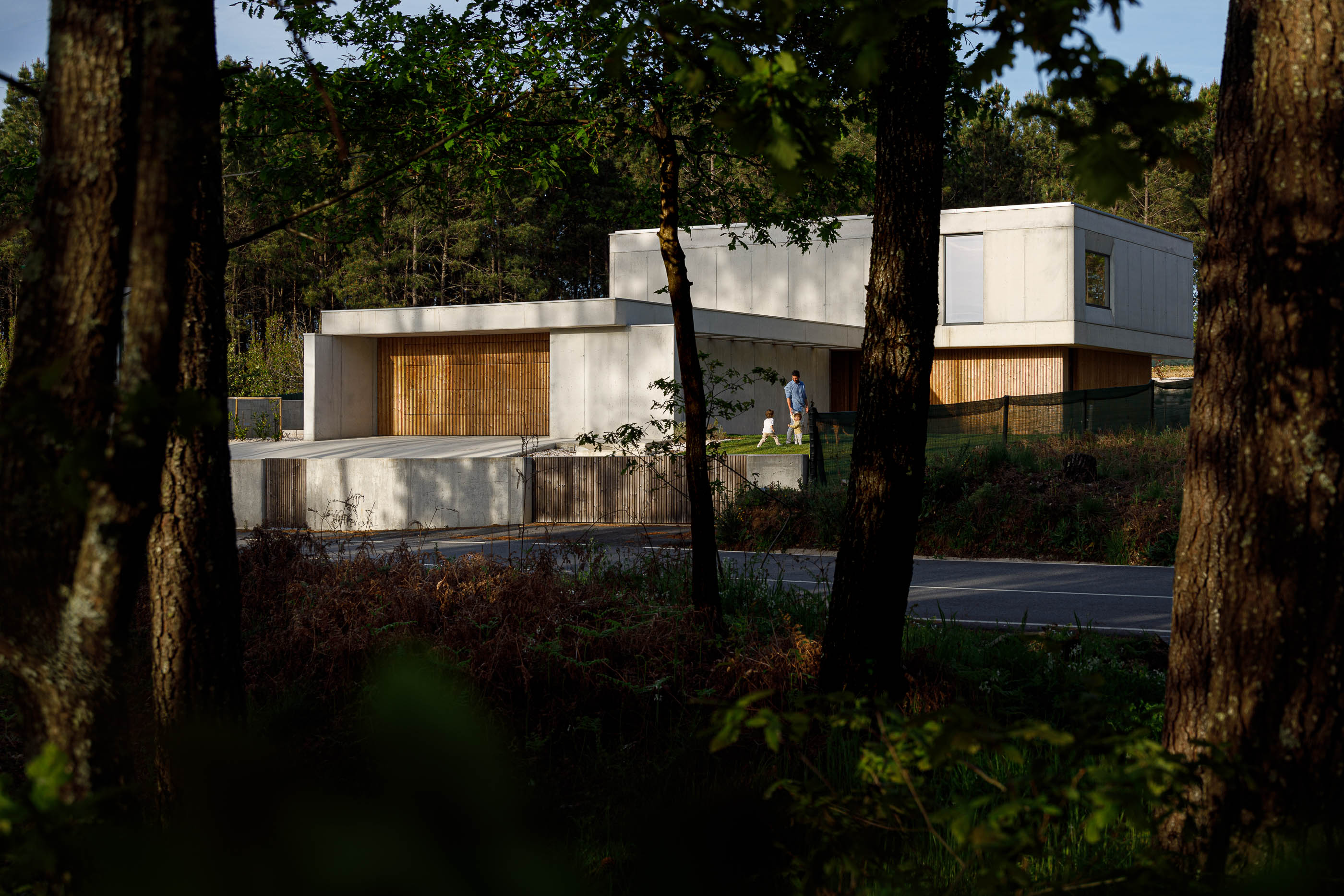 Exterior: Vista da casa moderna em betão e madeira, rodeada por árvores. — Casa em Mundão arquitetura Um para Um, arquitectura e engenharia em Viseu