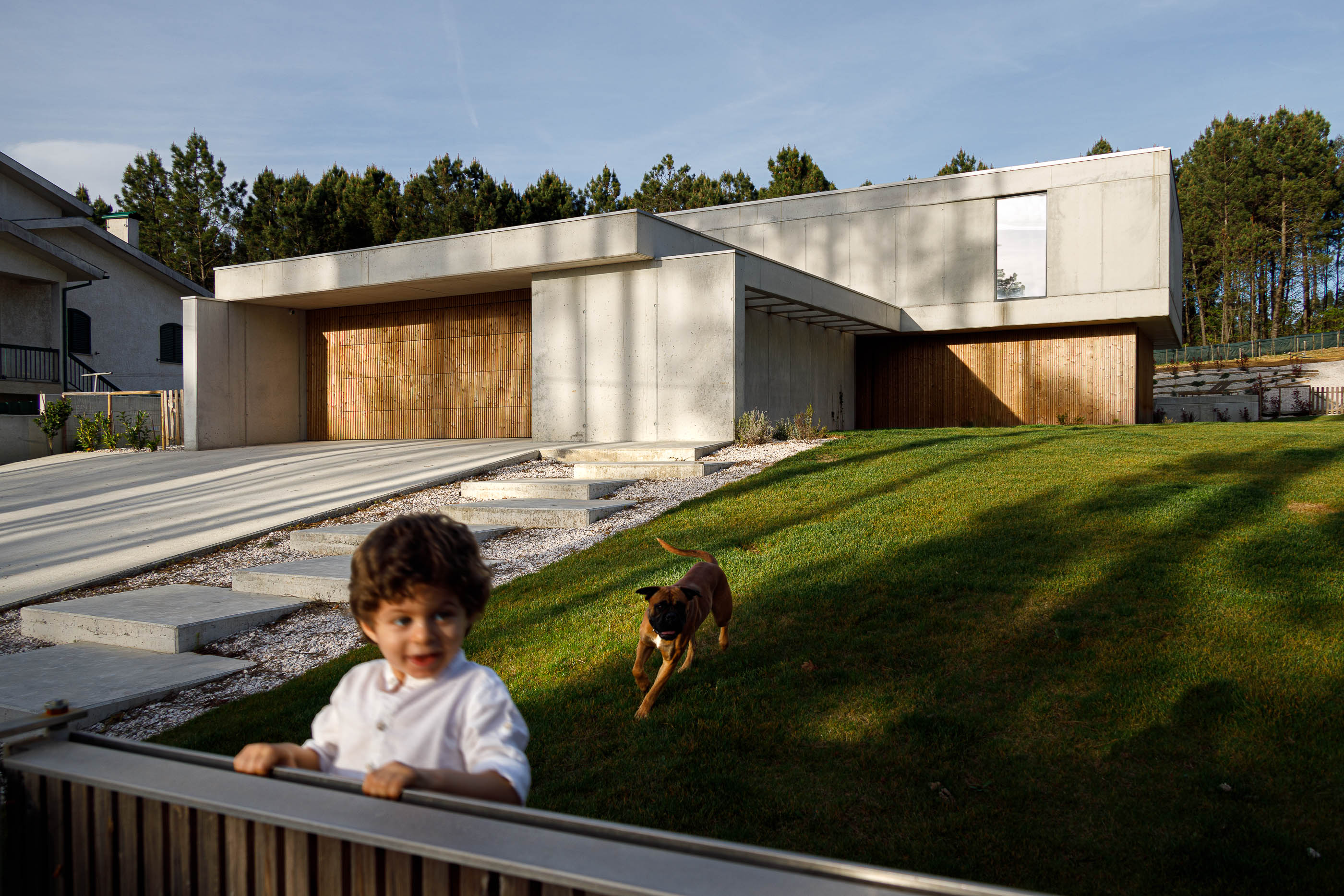 Exterior: Casa moderna com criança e cão no relvado e detalhes em betão. — Casa em Mundão arquitetura Um para Um, arquitectura e engenharia em Viseu