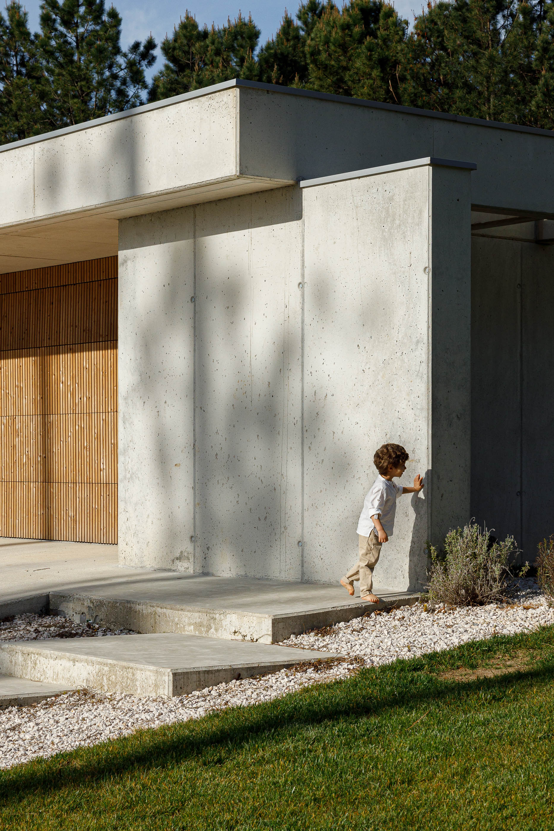Entrada: Detalhe da entrada da casa com criança a tocar na parede de betão. — Casa em Mundão arquitetura Um para Um, arquitectura e engenharia em Viseu
